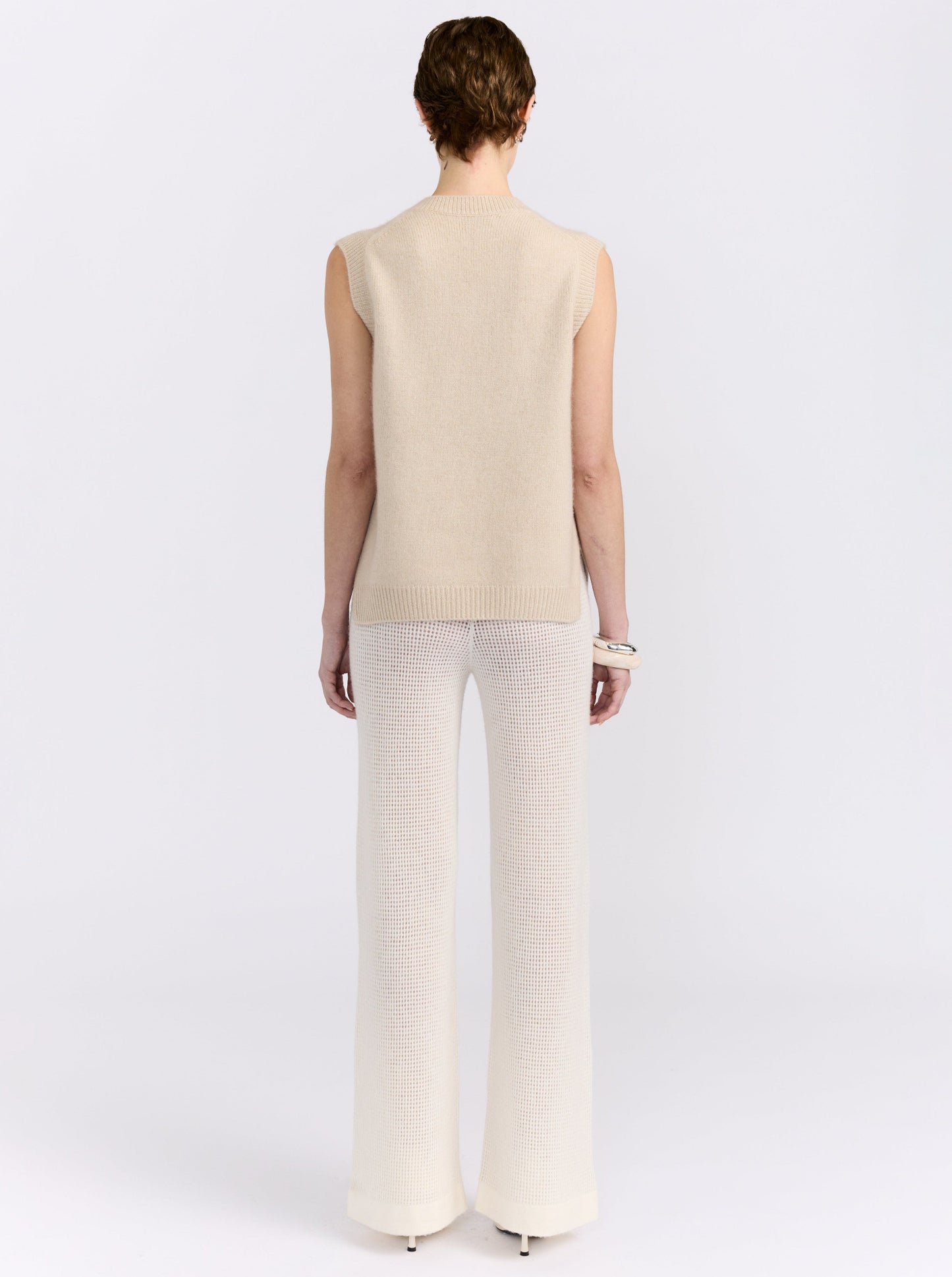 Beige cashmere vest with hand-embroidered floral detailing, styled with black wide-leg trousers.