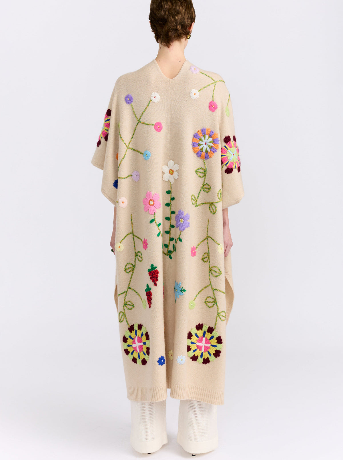 Back view of model wearing midi length beige cashmere kaftan with embroidered coloured flowers worn with white cashmere knit pants.