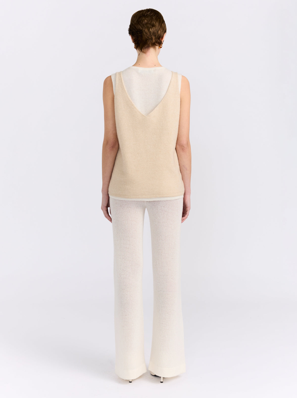 Back view model wearing the MANDKHAI beige and white double-layer cashmere vest with cream wide-leg trousers.
