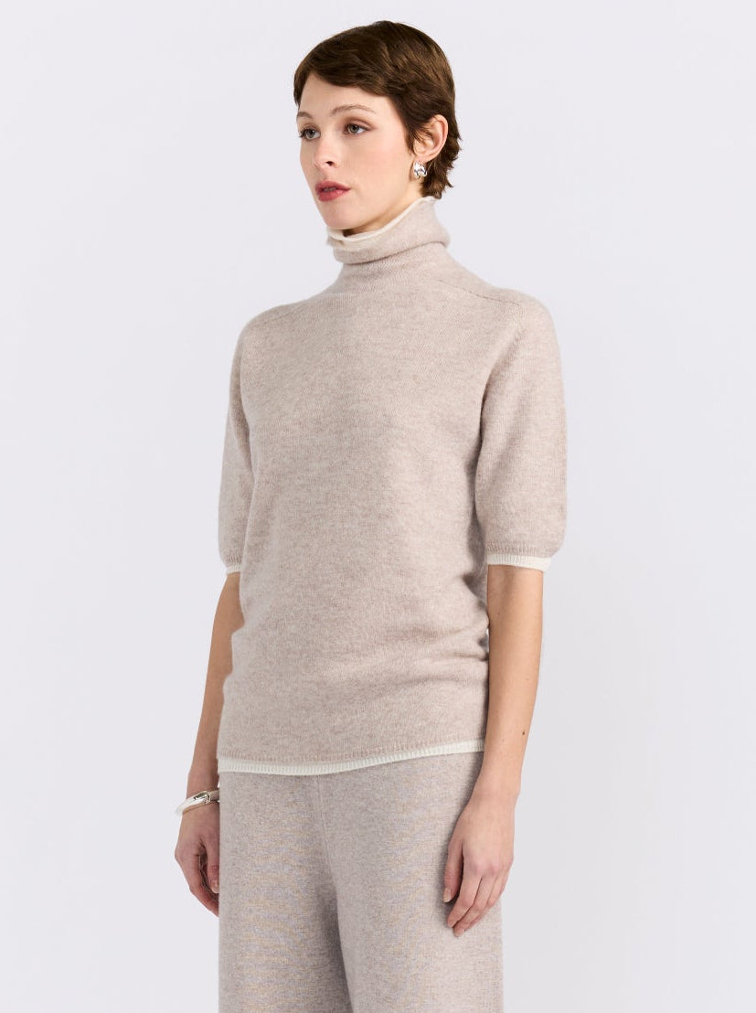 Cropped view model wearing beige knit turtleneck sweater with short sleeves and matching wide-leg trousers against white background.