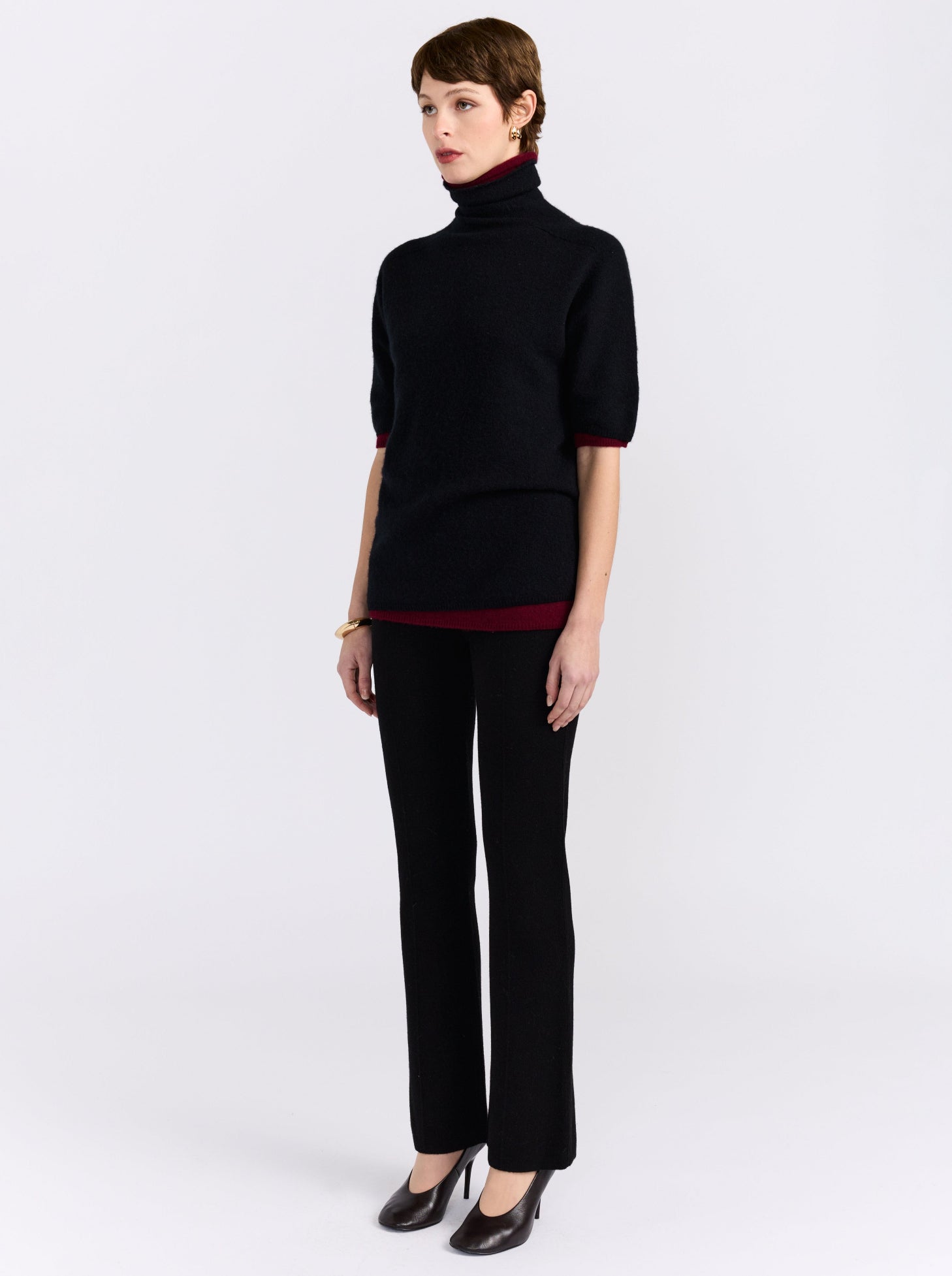 Side angle full length view model wearing black long tailored pants, with black short sleeve sweater and high heel pumps.
