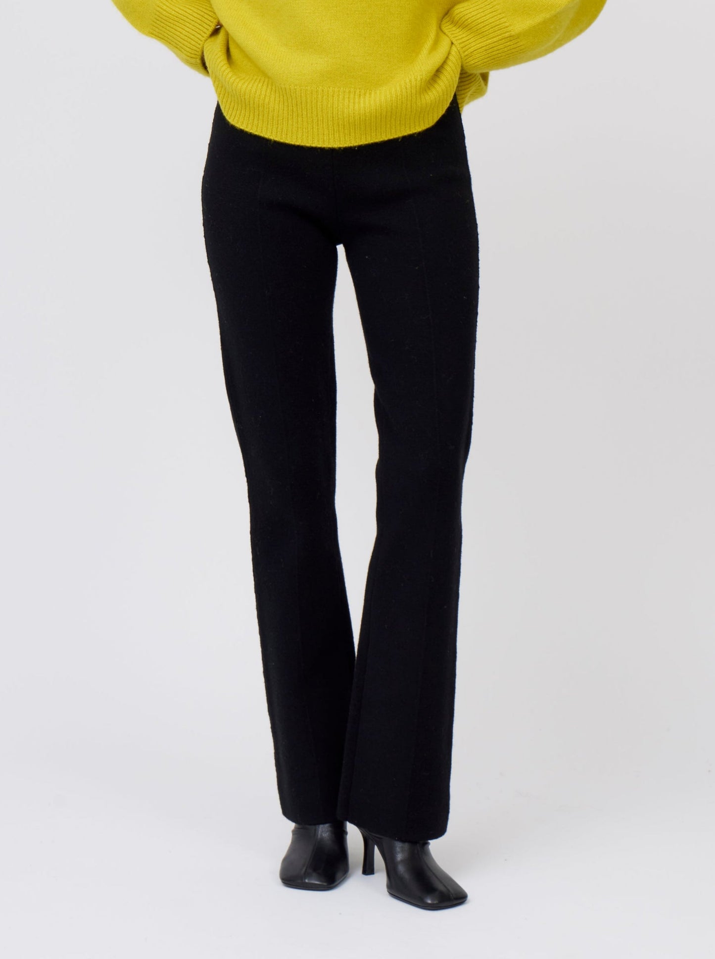 cropped front view model wearing black long tailored pants, with with slight boot cut flare, with yellow sweater and and high heel black ankle boots
