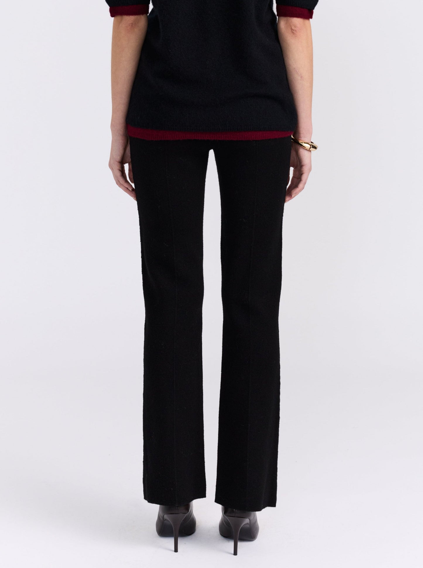 cropped back view model wearing black long tailored pants, with with slight boot cut flare, with black short sleeve sweater and and high heels.