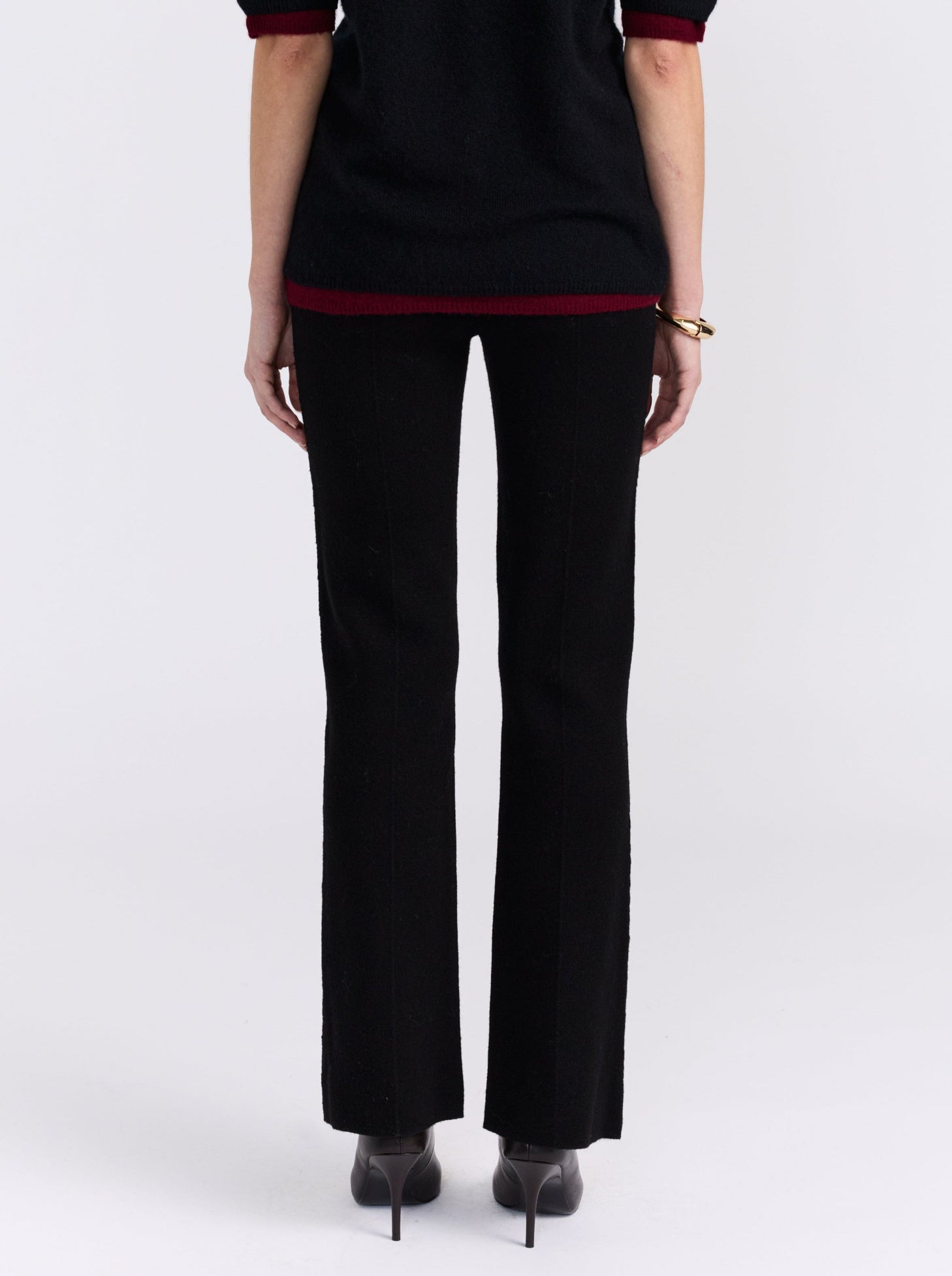 cropped back view model wearing black long tailored pants, with with slight boot cut flare, with black short sleeve sweater and and high heels.