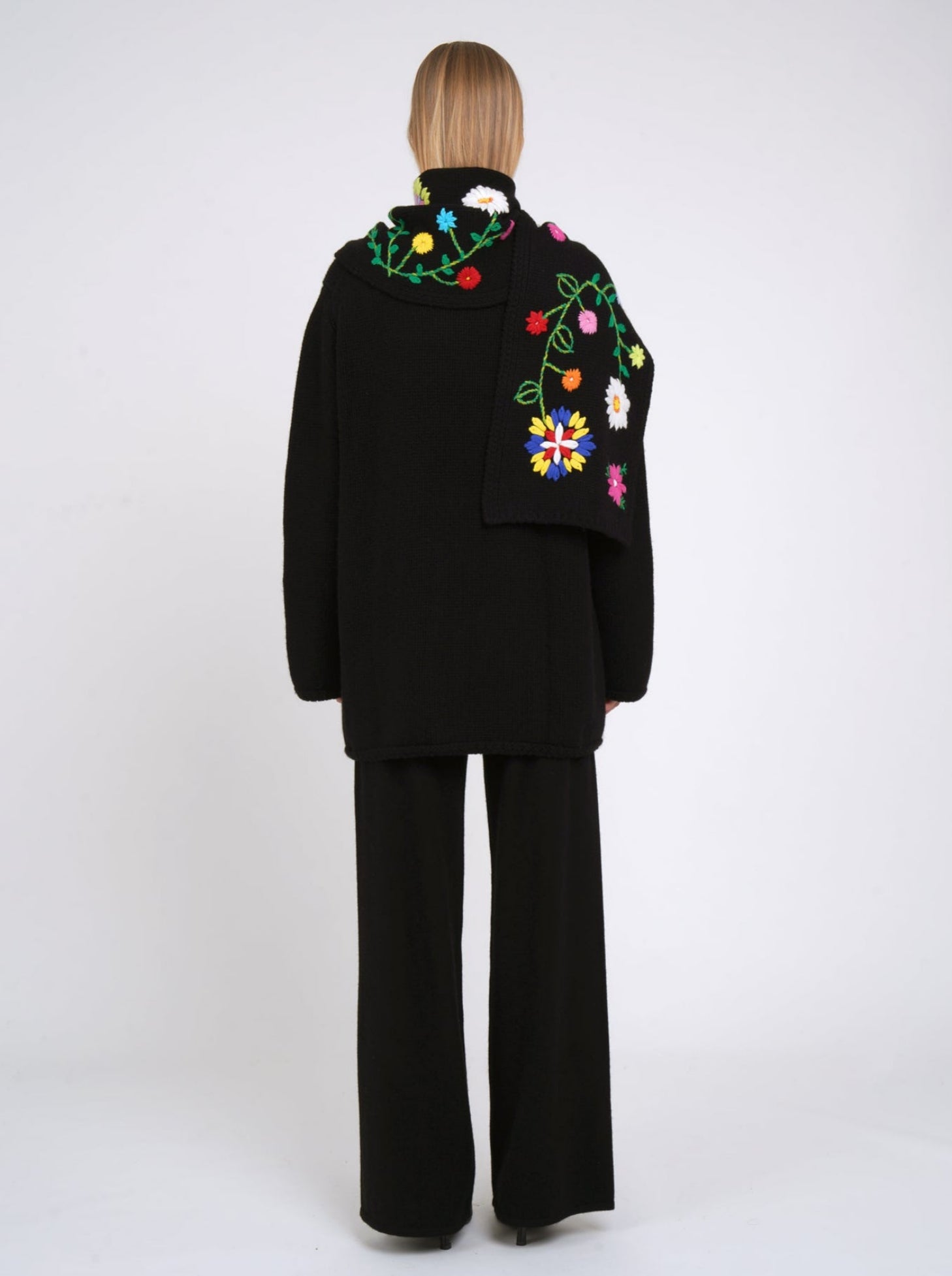 Back view of black cashmere hip length jacket with flower embroidered detachable scarf worn with black cashmere trousers.