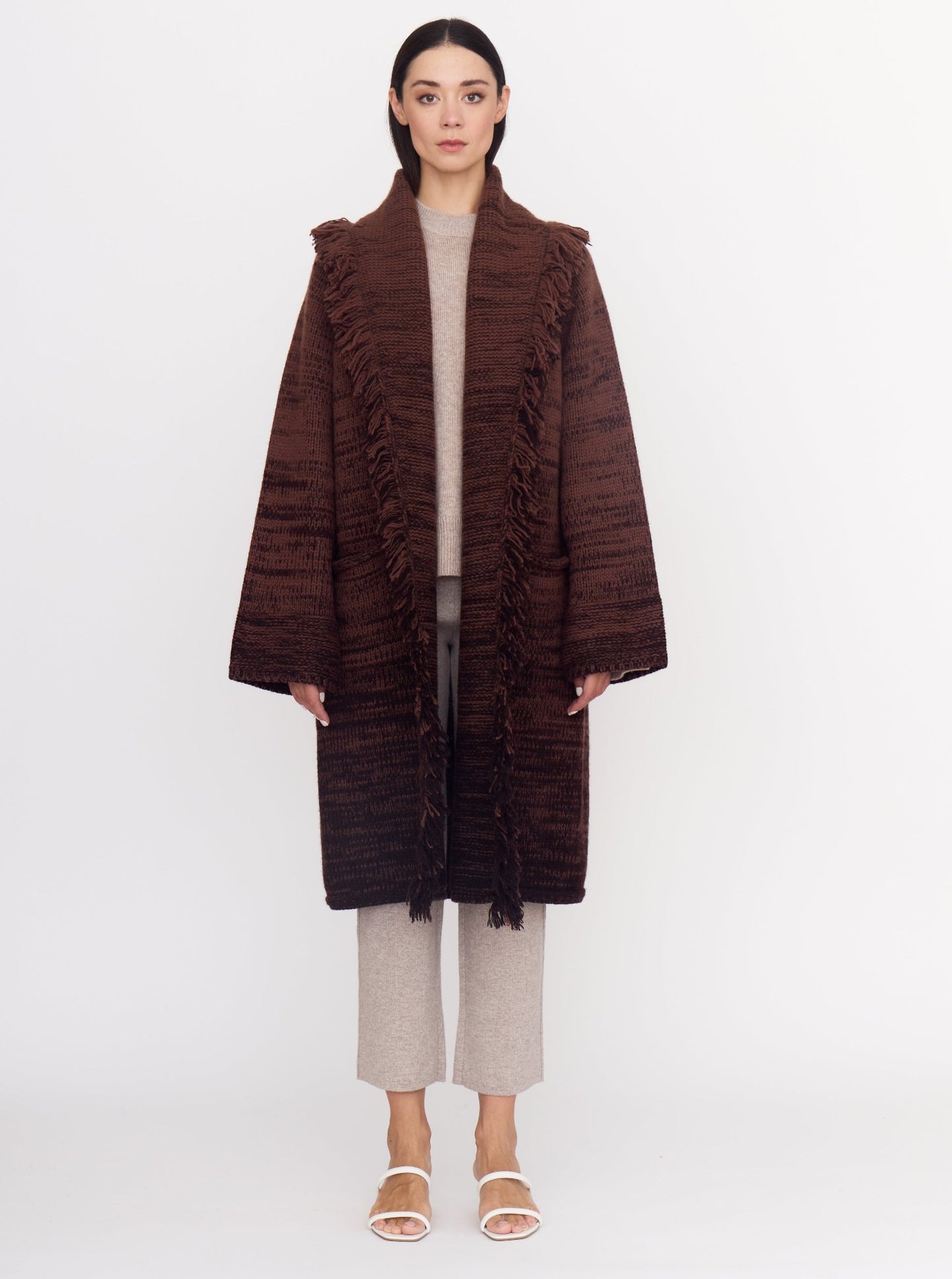 Model wearing knee length cashmere chunky knit coat in a mix of two shades of chocolate brown; wearing with beige cashmere cropped pants and top.