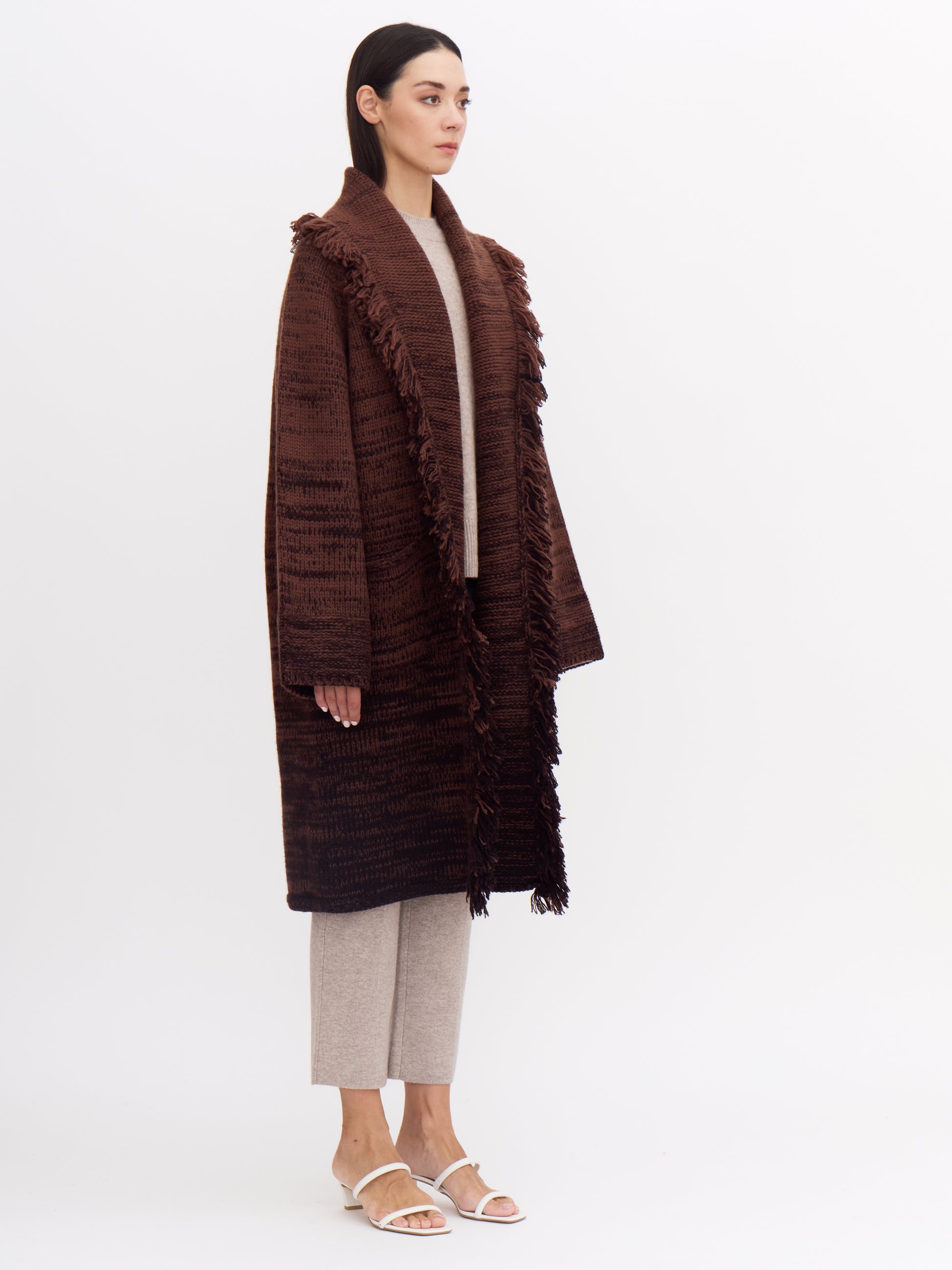 Side view of model wearing knee length brown cashmere knit coat, showing full length generous sleeves.