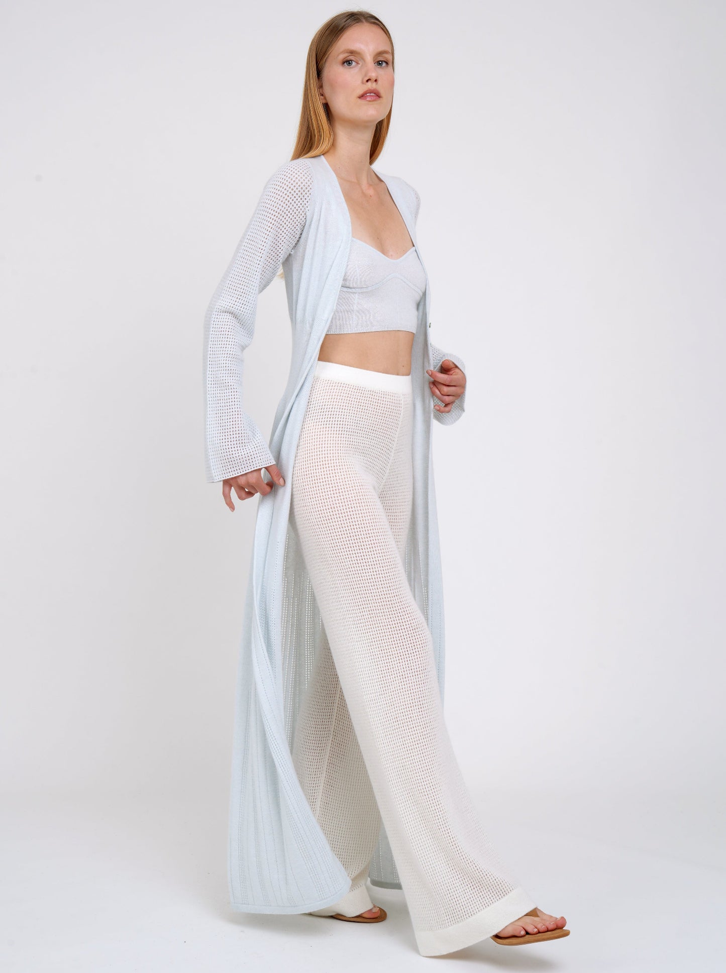 Model walking in pale blue knit cropped bra top and matching blue cashmere long cardigan with white knit trousers.