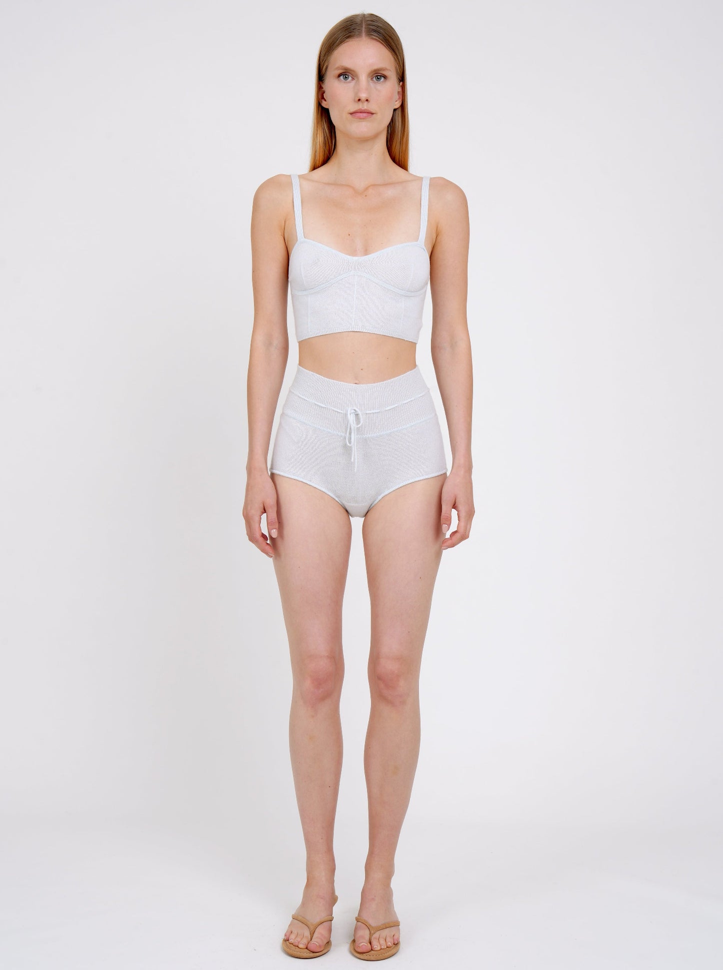 Standing model wears pale blue cashmere shorts with drawstring waist and matching pale blue knit  cropped bra top.