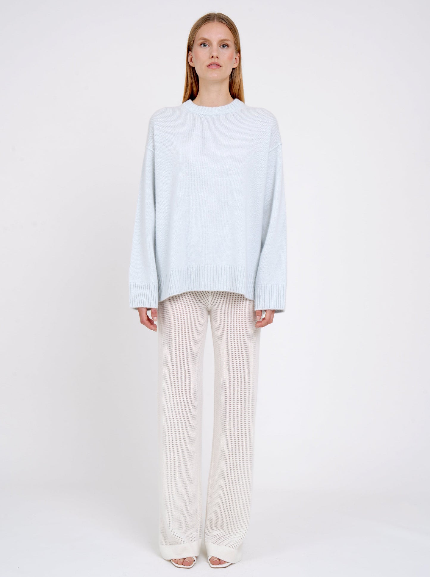 Front view model in light blue long jumper with round neck, long sleeves and white cashmere knit pants.