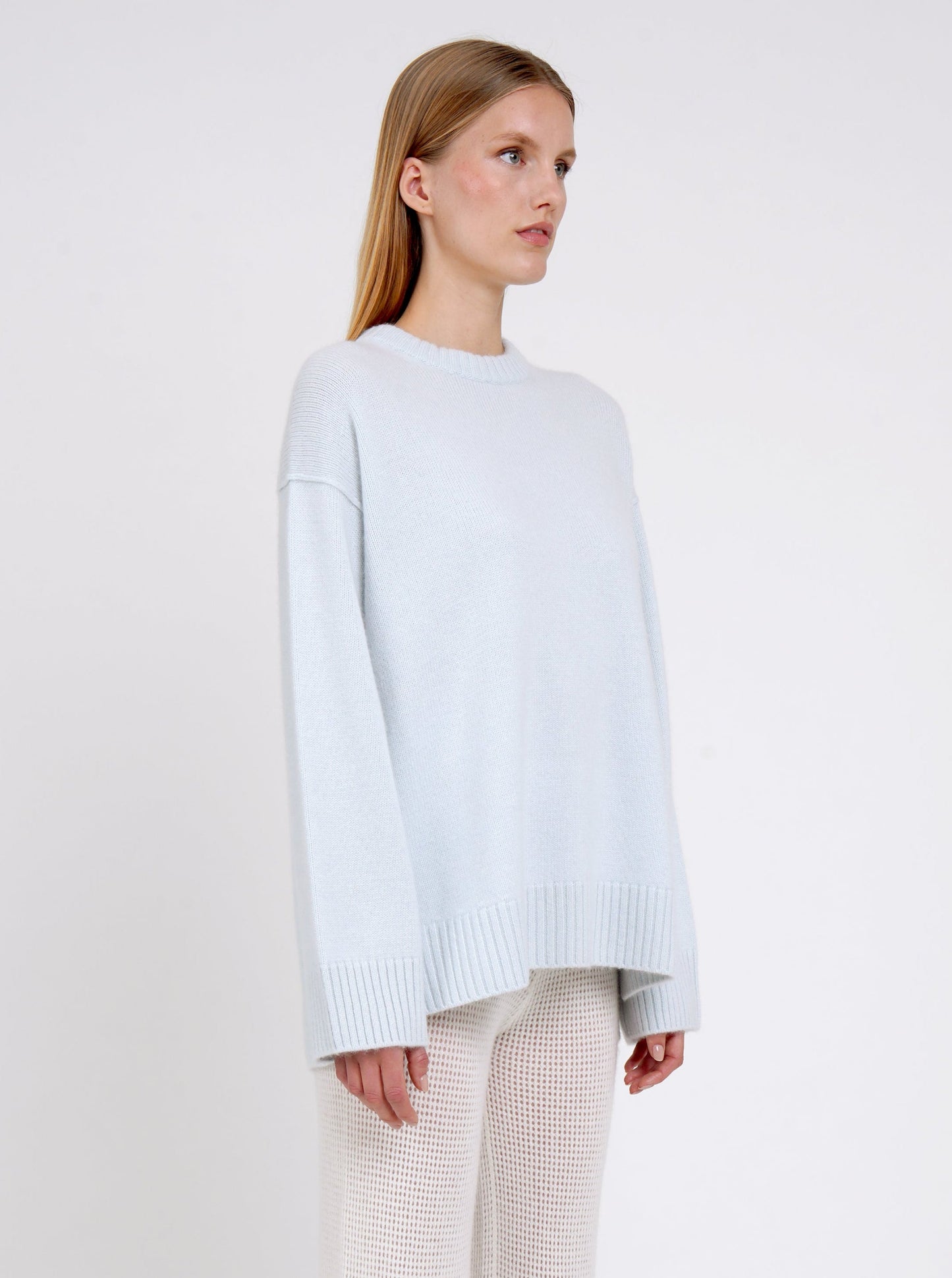 Close up side view model in light blue long jumper with round neck, long sleeves and white cashmere knit pants.
