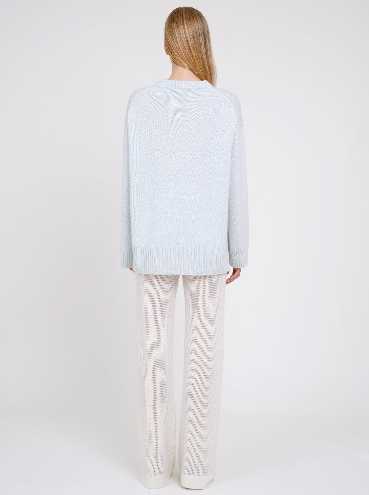 Back view model in light blue long jumper with round neck, long sleeves and white cashmere knit pants.