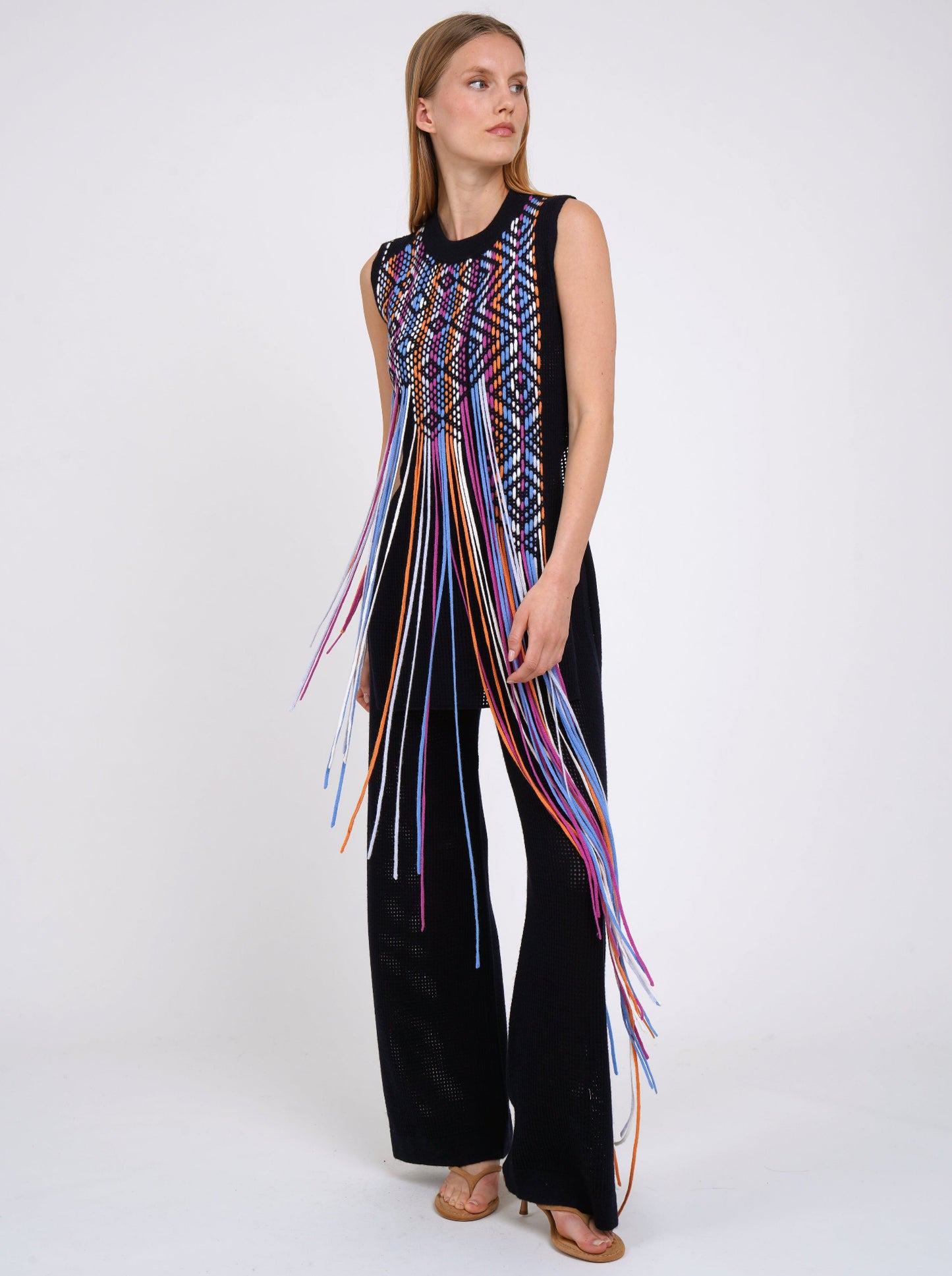 dark navy net knit pants worn with light weight cashmere knit sleeveless tunic decorated with woven coloured fringes.