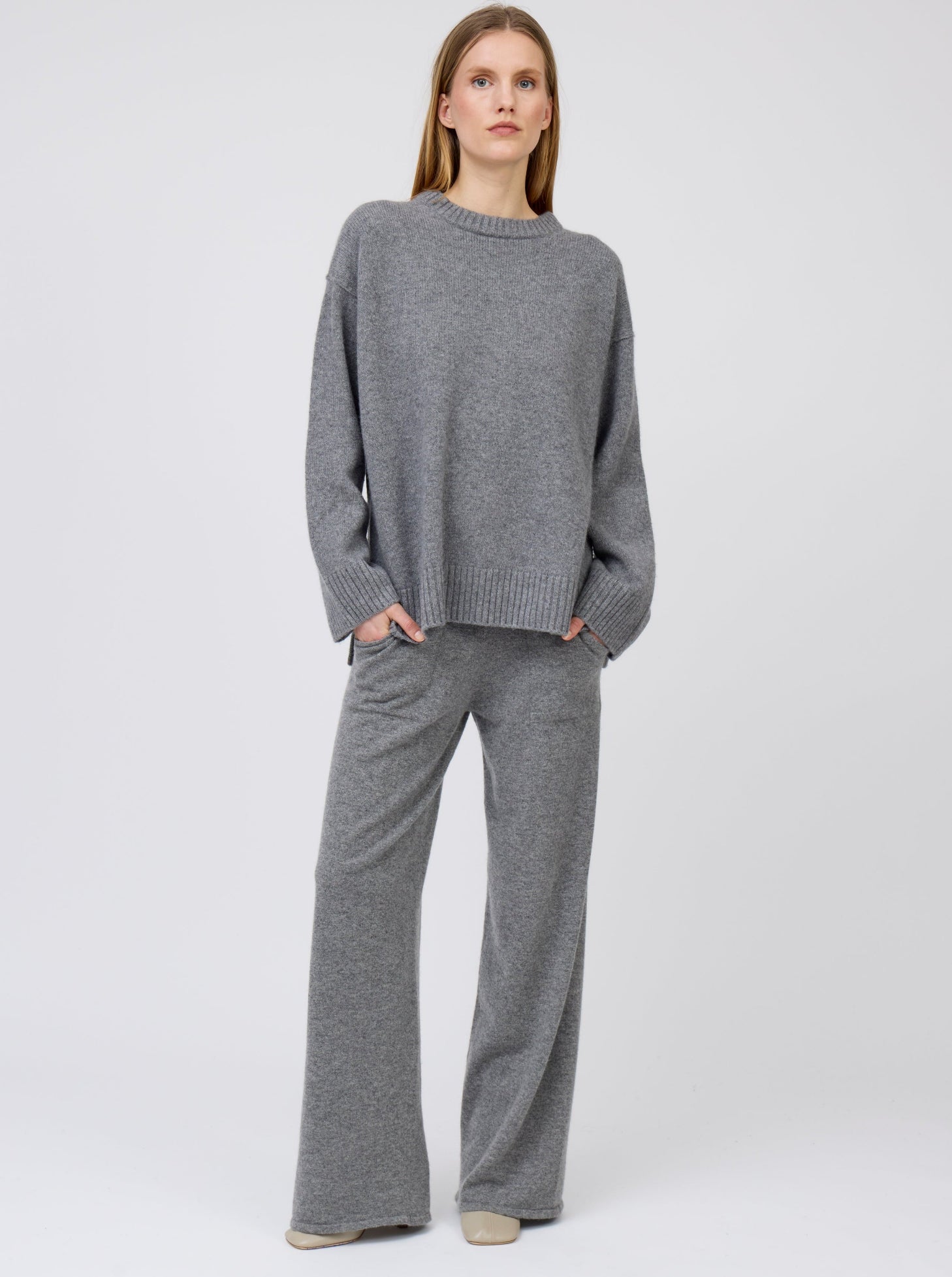 Front view of model wearing grey cashmere, wide leg pants with pockets; worn with matching grey cashmere round neck oversize sweater.