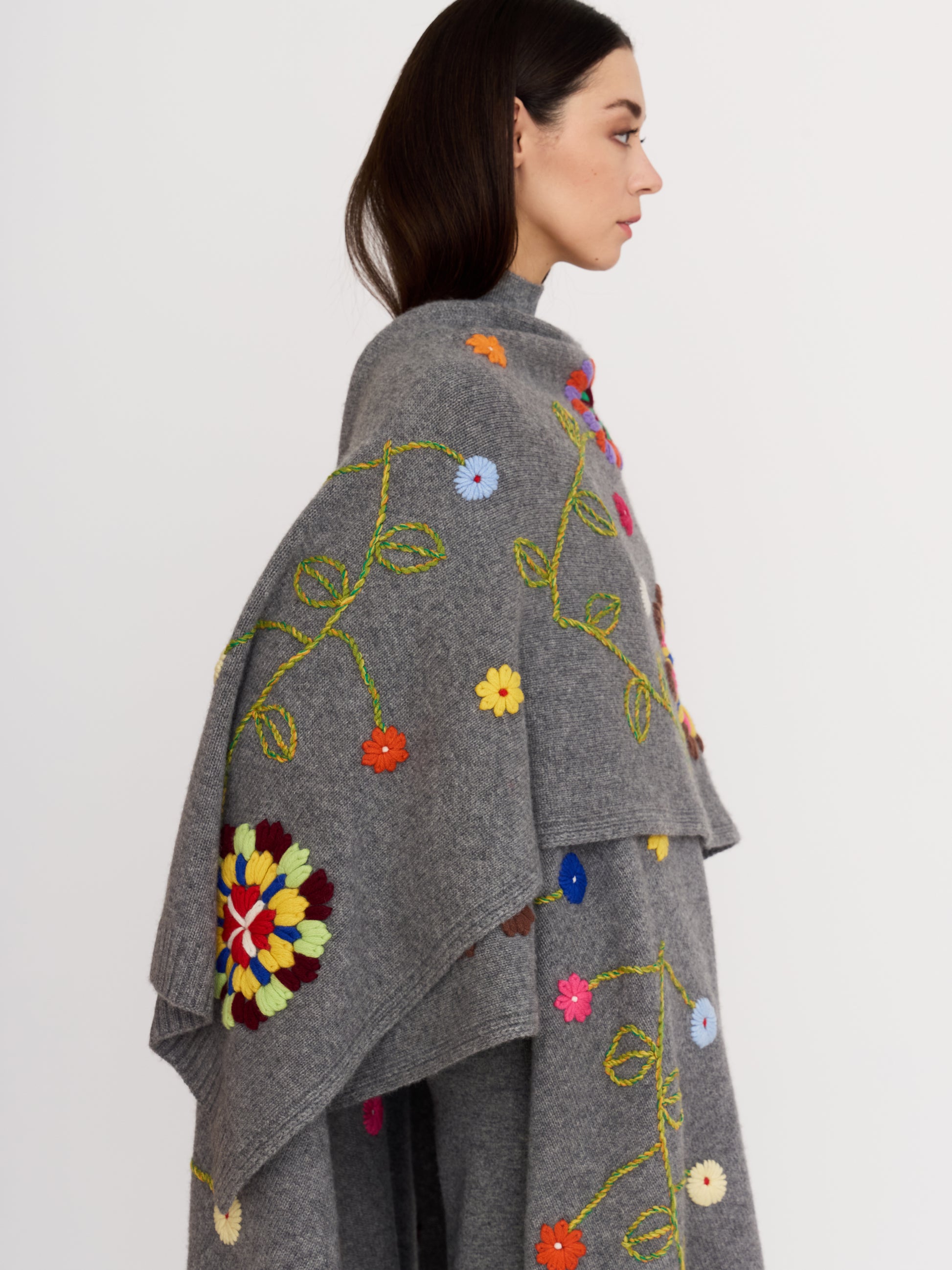 Side view of model wearing grey cashmere shawl hand embroidered with bright, multicoloured flowers.