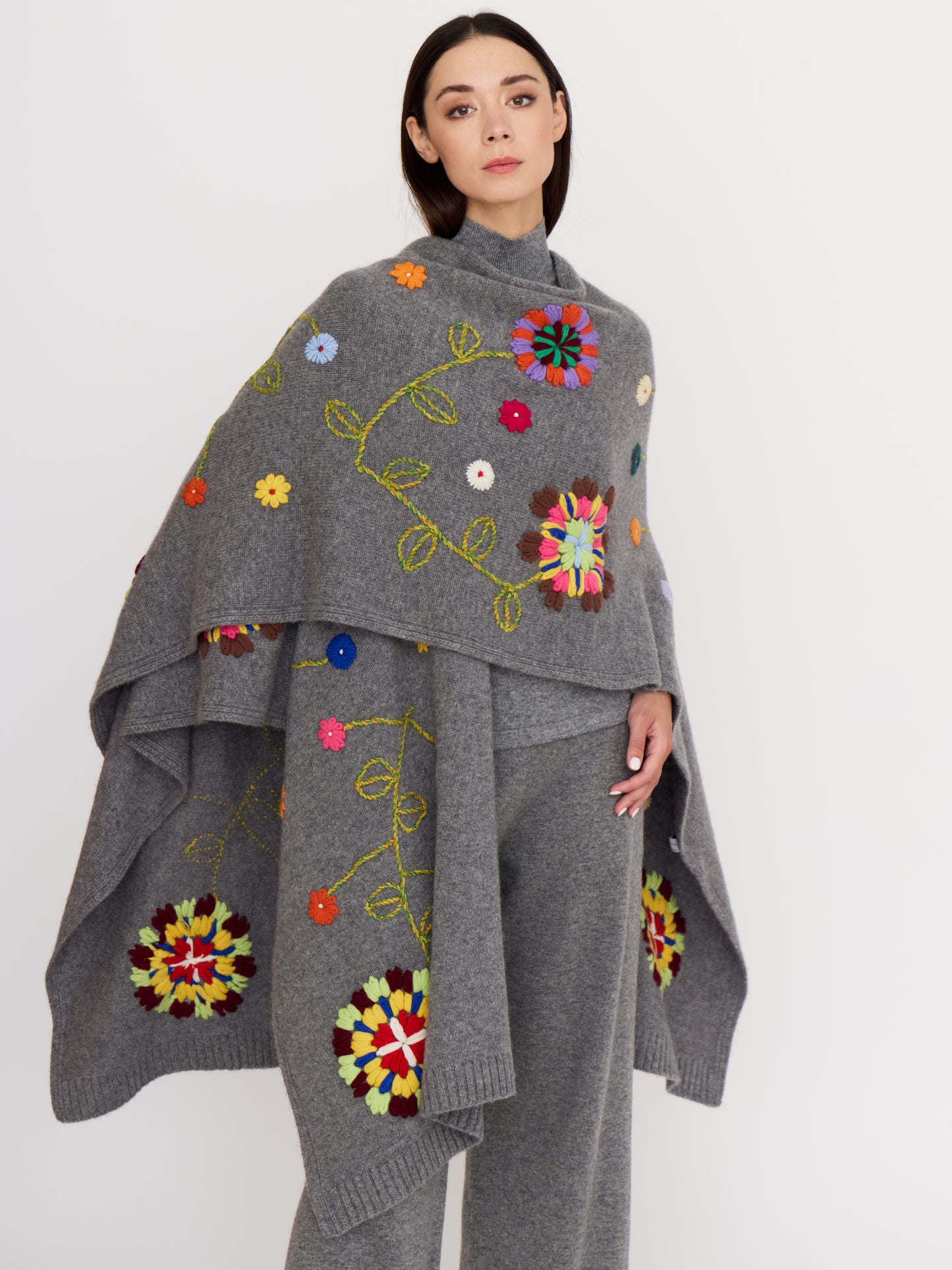 Model wearing voluminous grey cashmere shawl covered with bright, multi-coloured hand embroidered flowers.