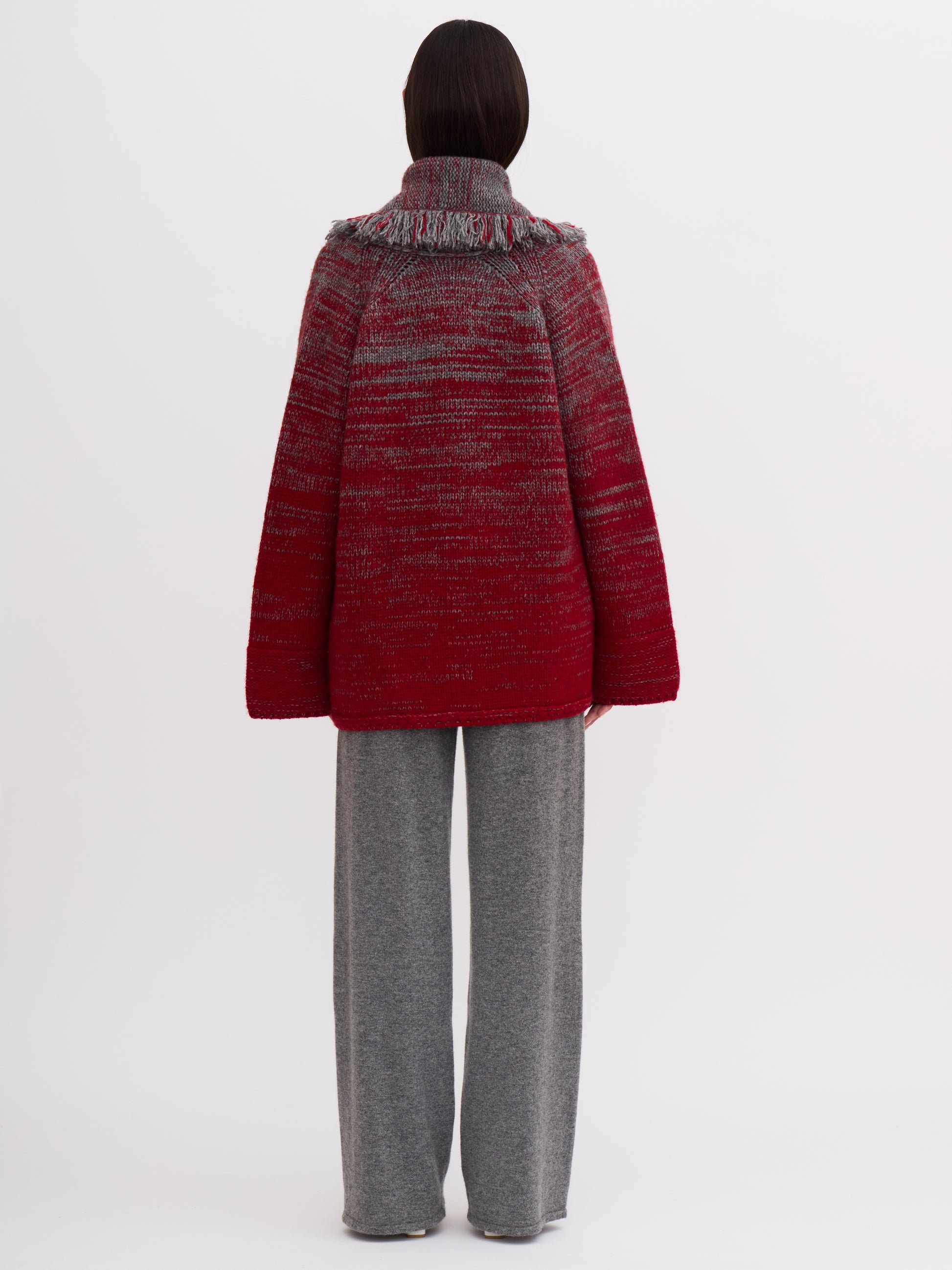 Back view of model wearing chunky knit cashmere jacket in grey and red mix; with grey wide leg cashmere pants.