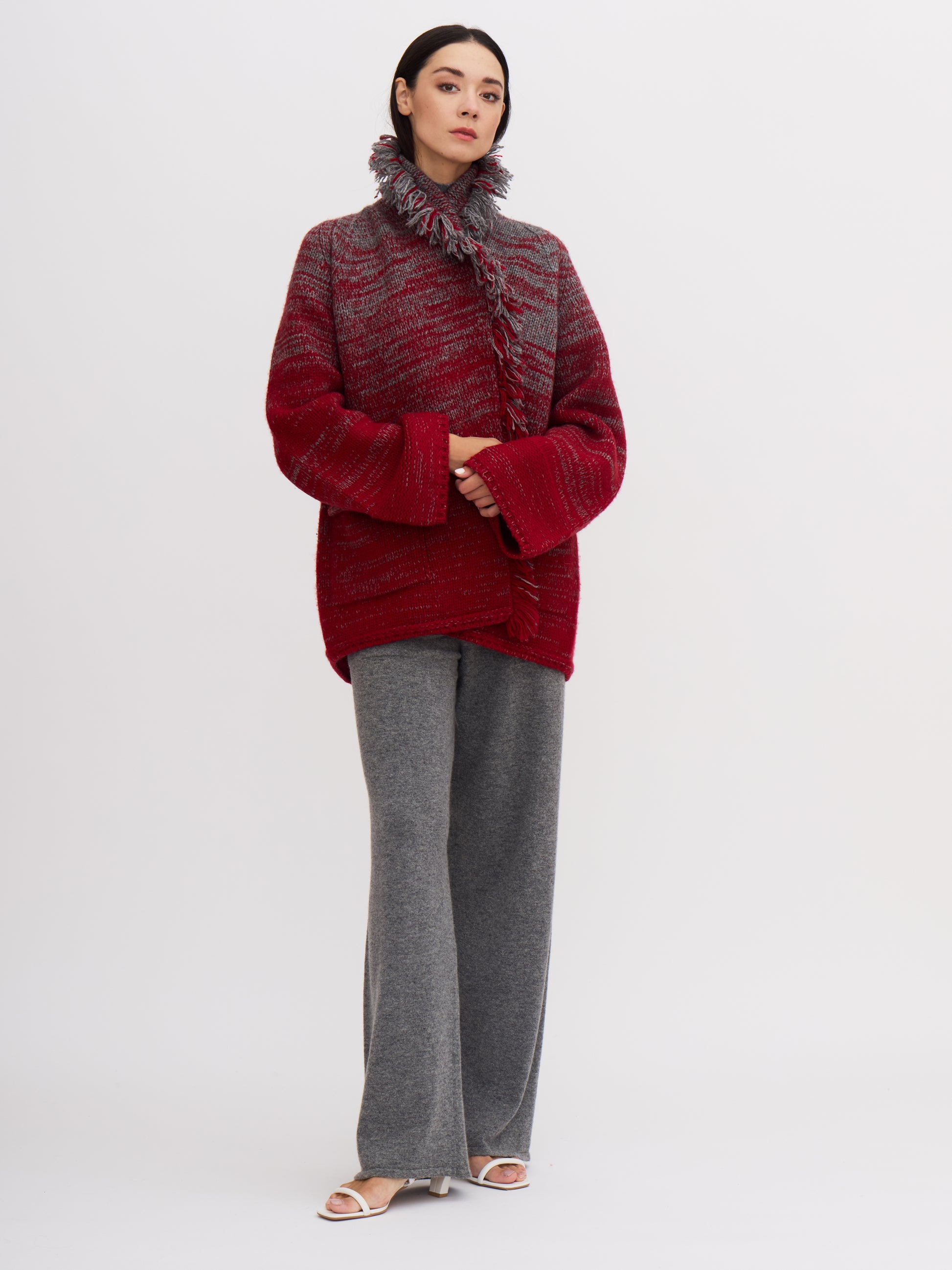 Model wrapped in chunky knit jacket in grey and red cashmere with fringed collar turned up.