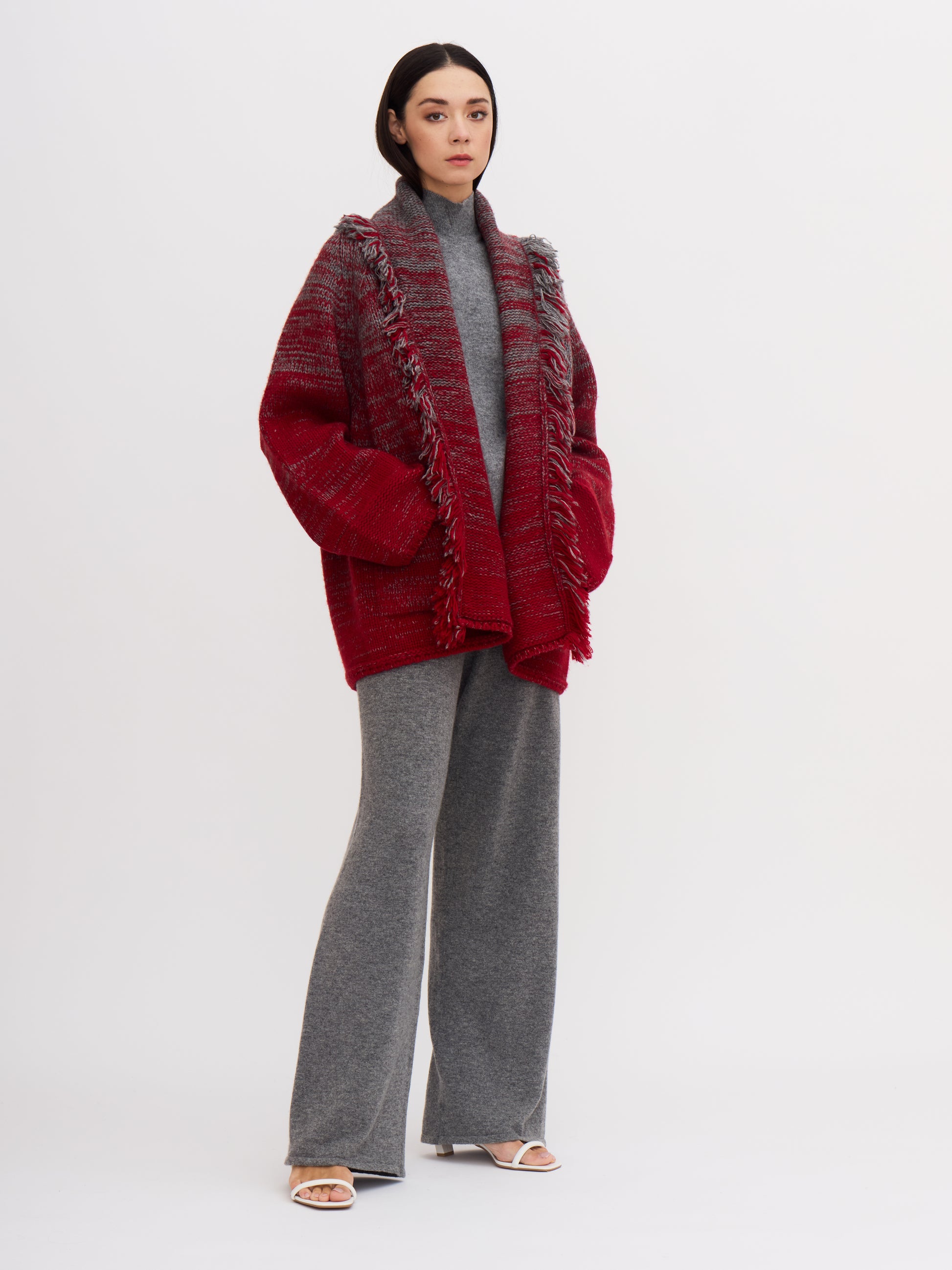 Model wearing grey and red cashmere jacket with fringed shawl collar, with grey wide leg cashmere pants and grey turtle neck top.