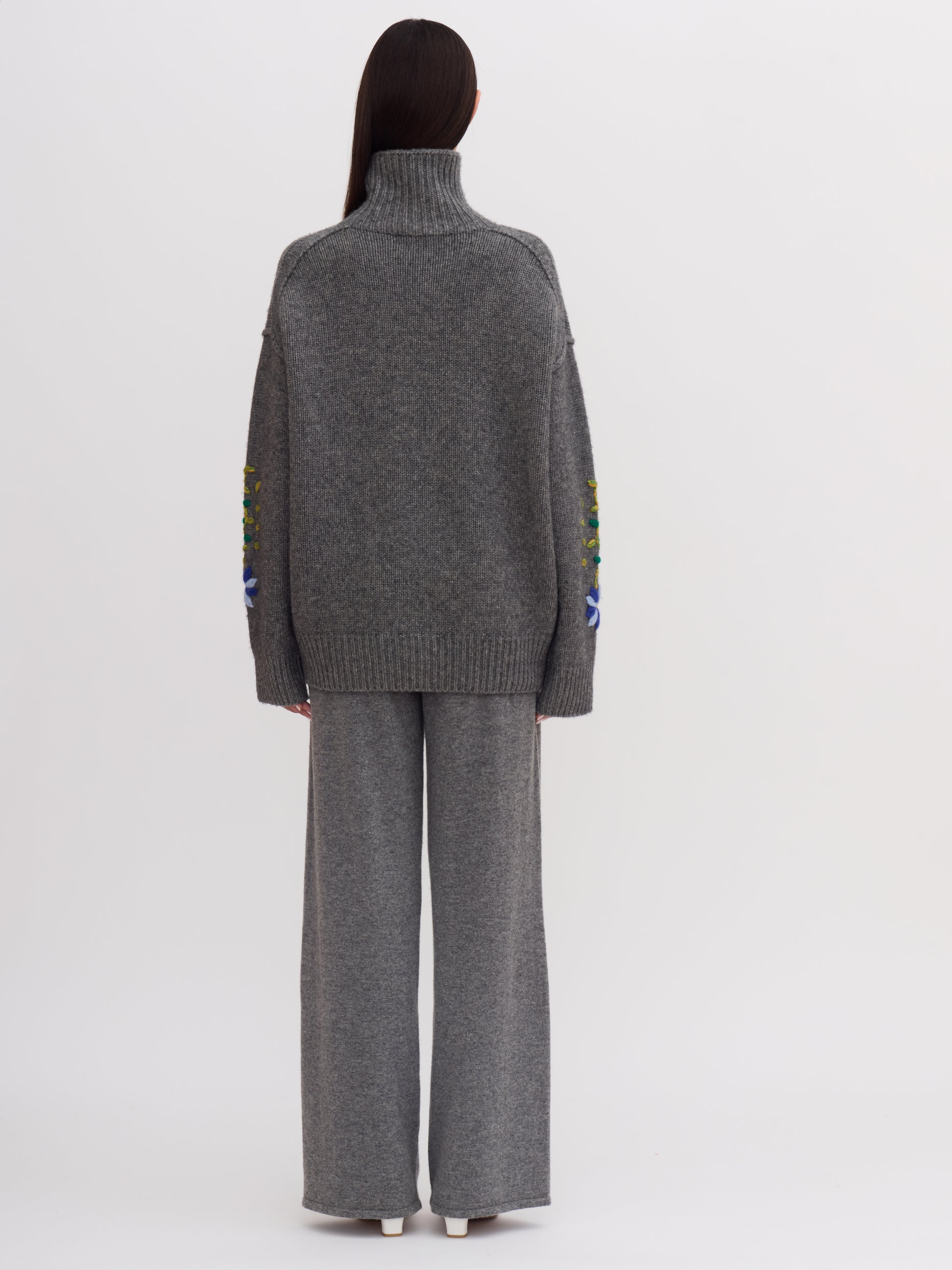 Back view of model wearing grey cashmere roll neck jumper and matching grey cashmere wide leg pants.