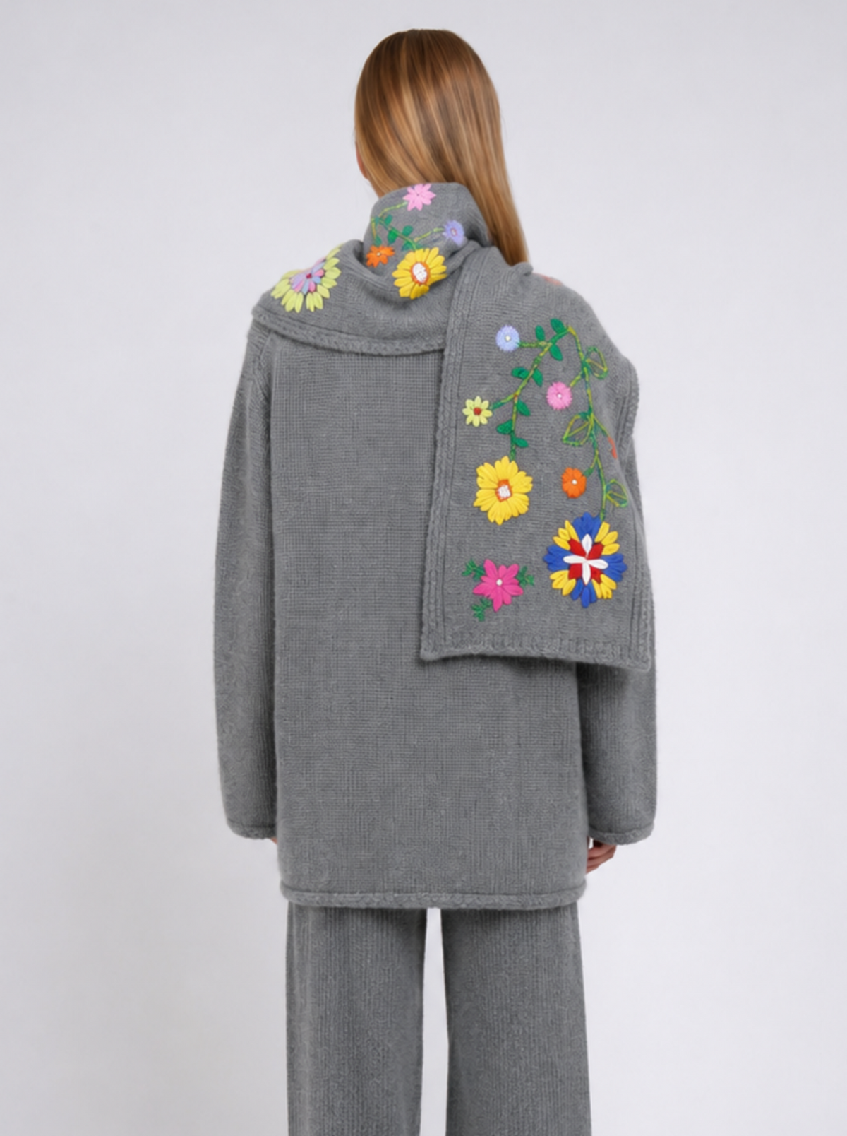 Back view model wearing a grey cashmere jacket with a colourful scarf with embroidered flowers, worn with matching grey wide-leg trousers, against a white background.