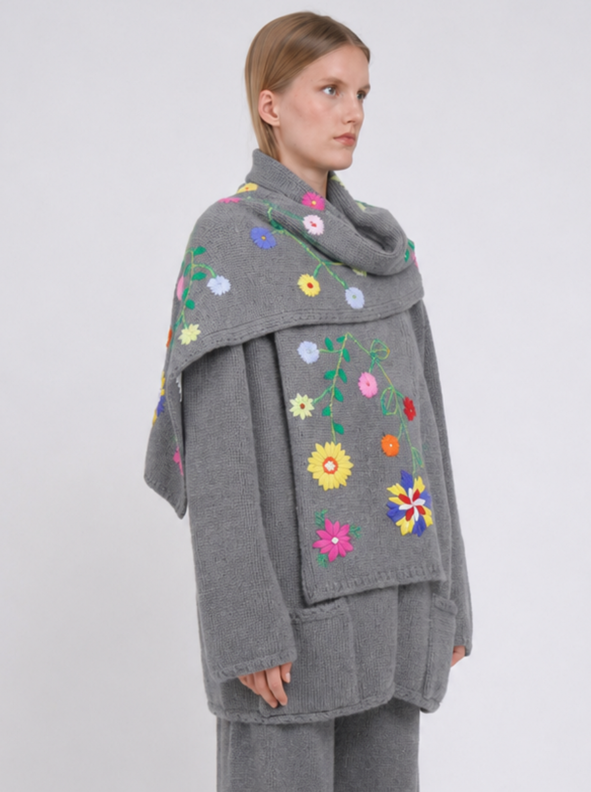 Side view model wearing a grey cashmere jacket  with colourful hand embroidered scarf, paired with matching grey wide-leg trousers, against white back ground.