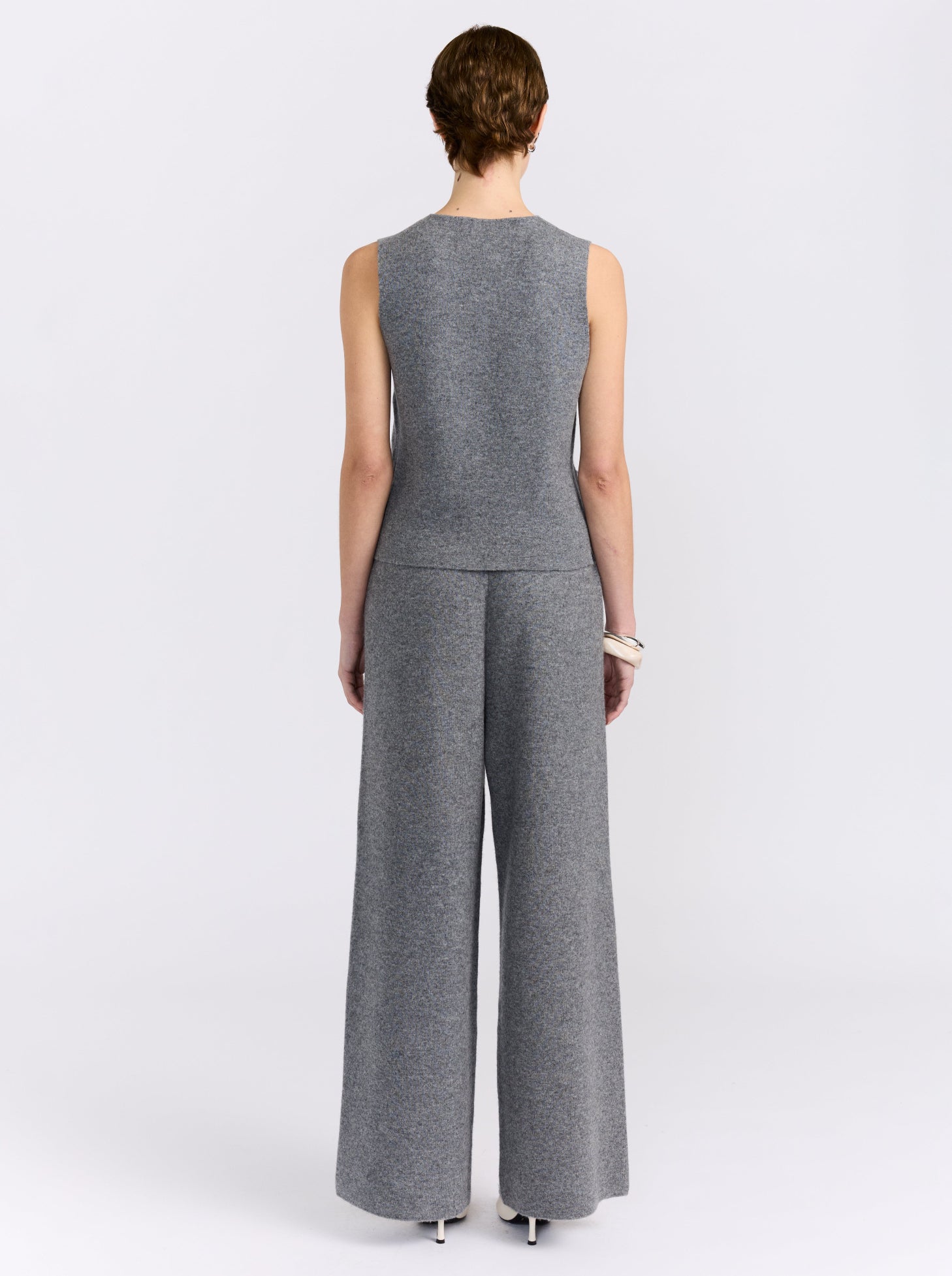 Back view model against white studio background wearing matching grey sleeveless waistcoat and wide-leg trousers set with white shoes