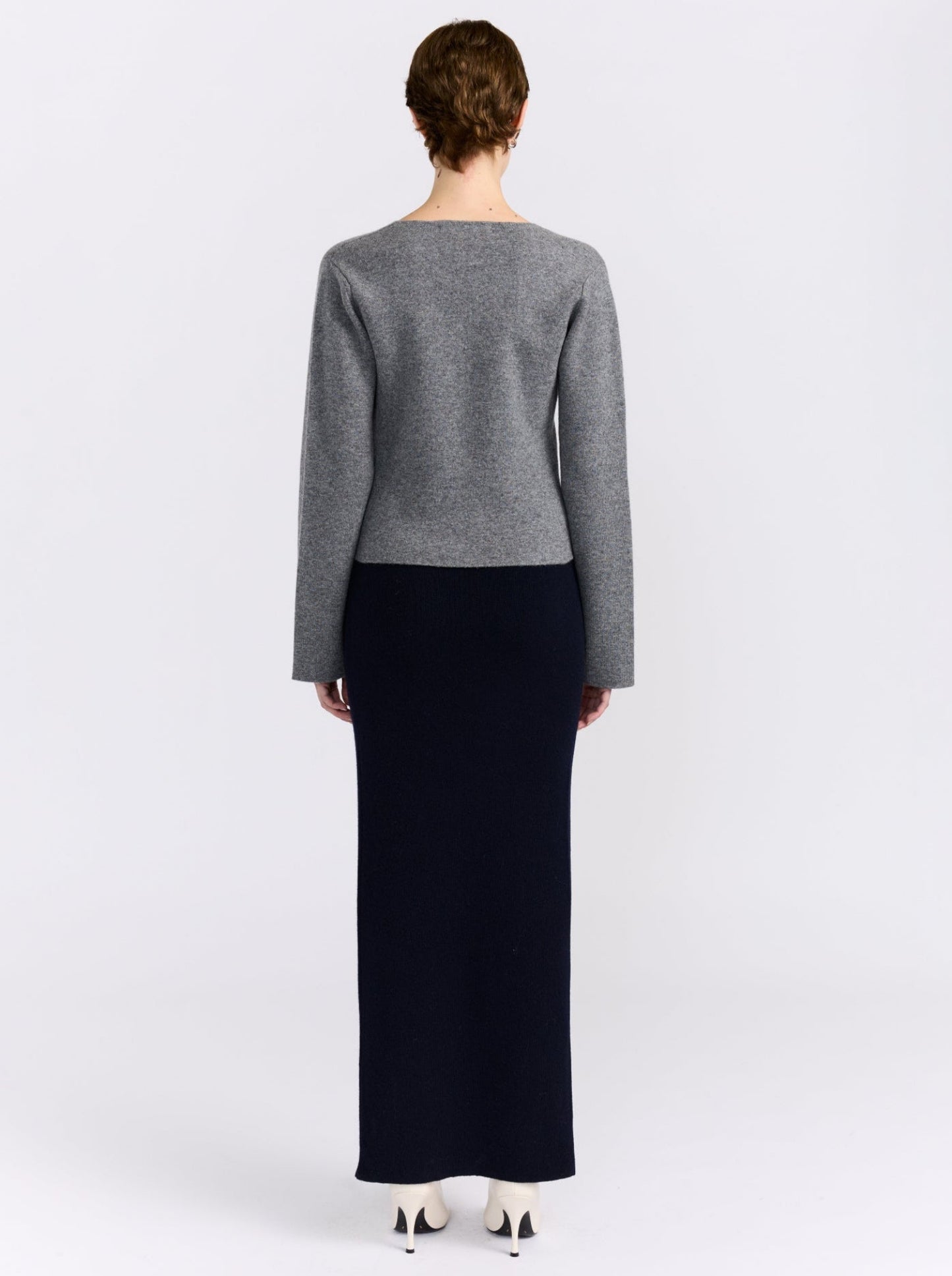 Back view model wears grey cashmere long sleeve cardigan with maxi length navy, straight skirt and white high heels.