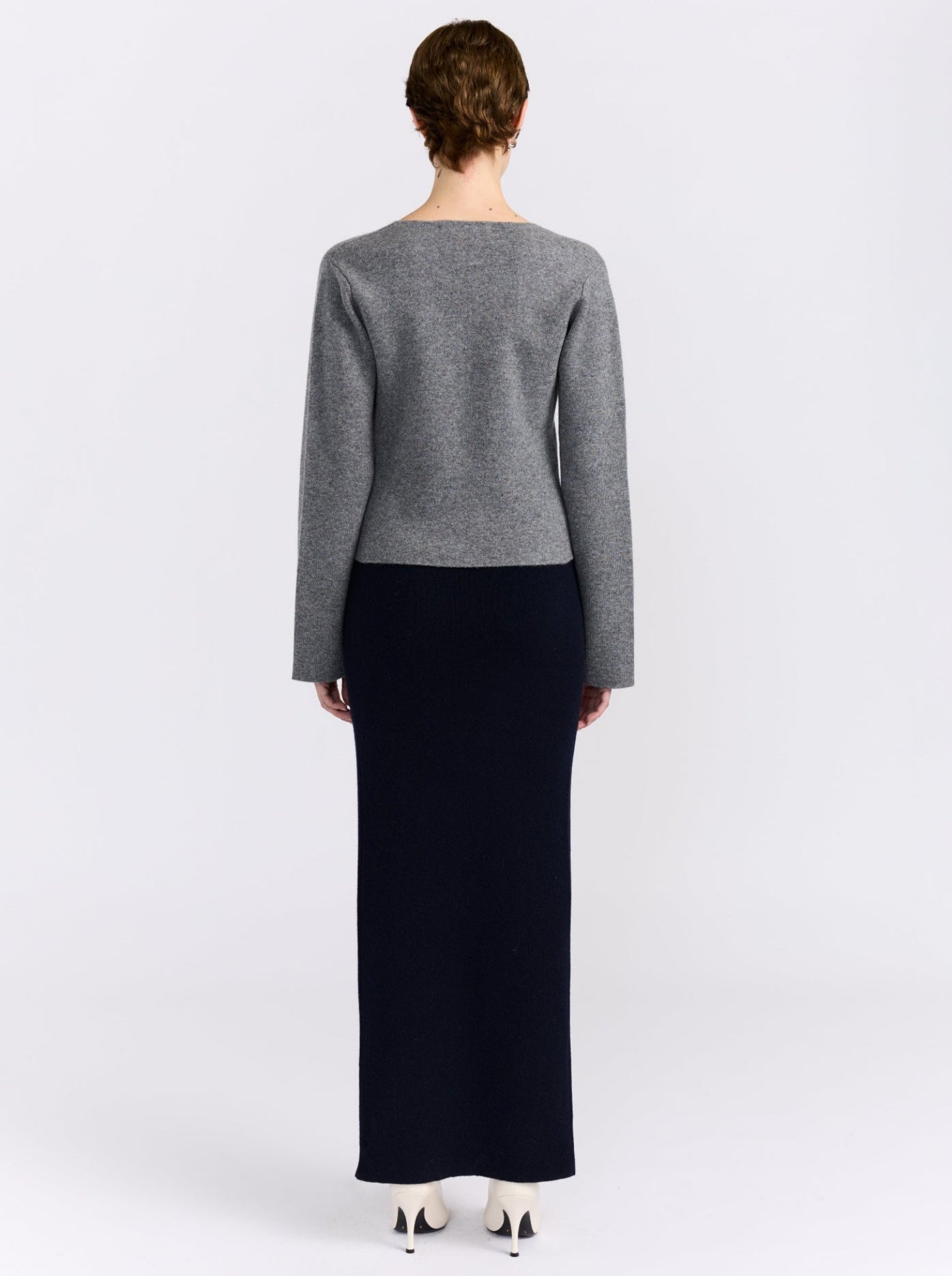 Back view model wears grey cashmere long sleeve cardigan with maxi length navy, straight skirt and white high heels.