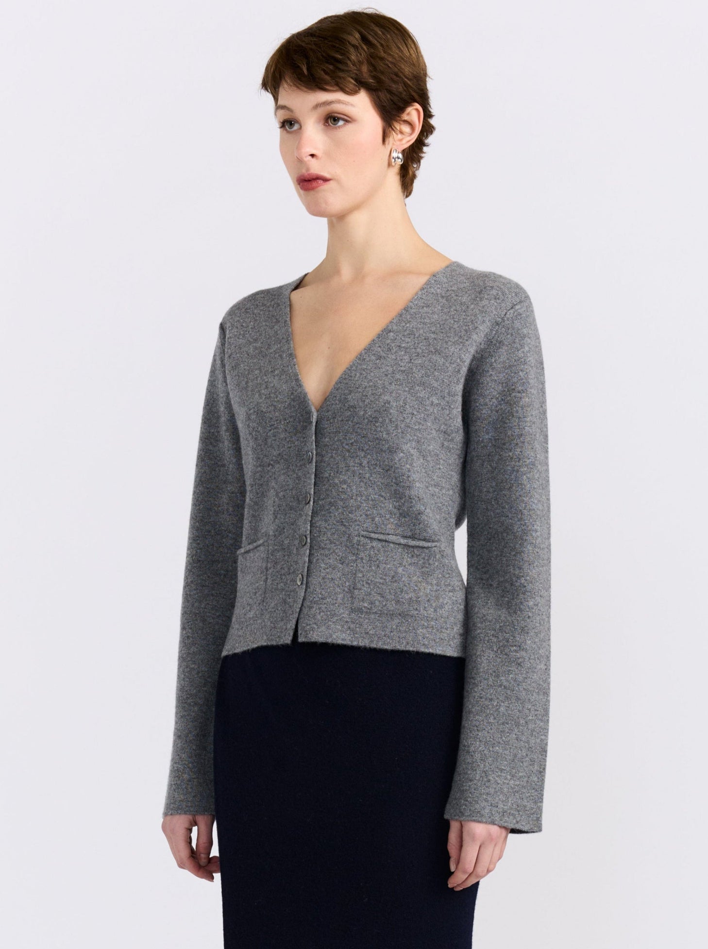 Close-up side view model wears grey cashmere v neck button front cardigan with navy, straight skirt.