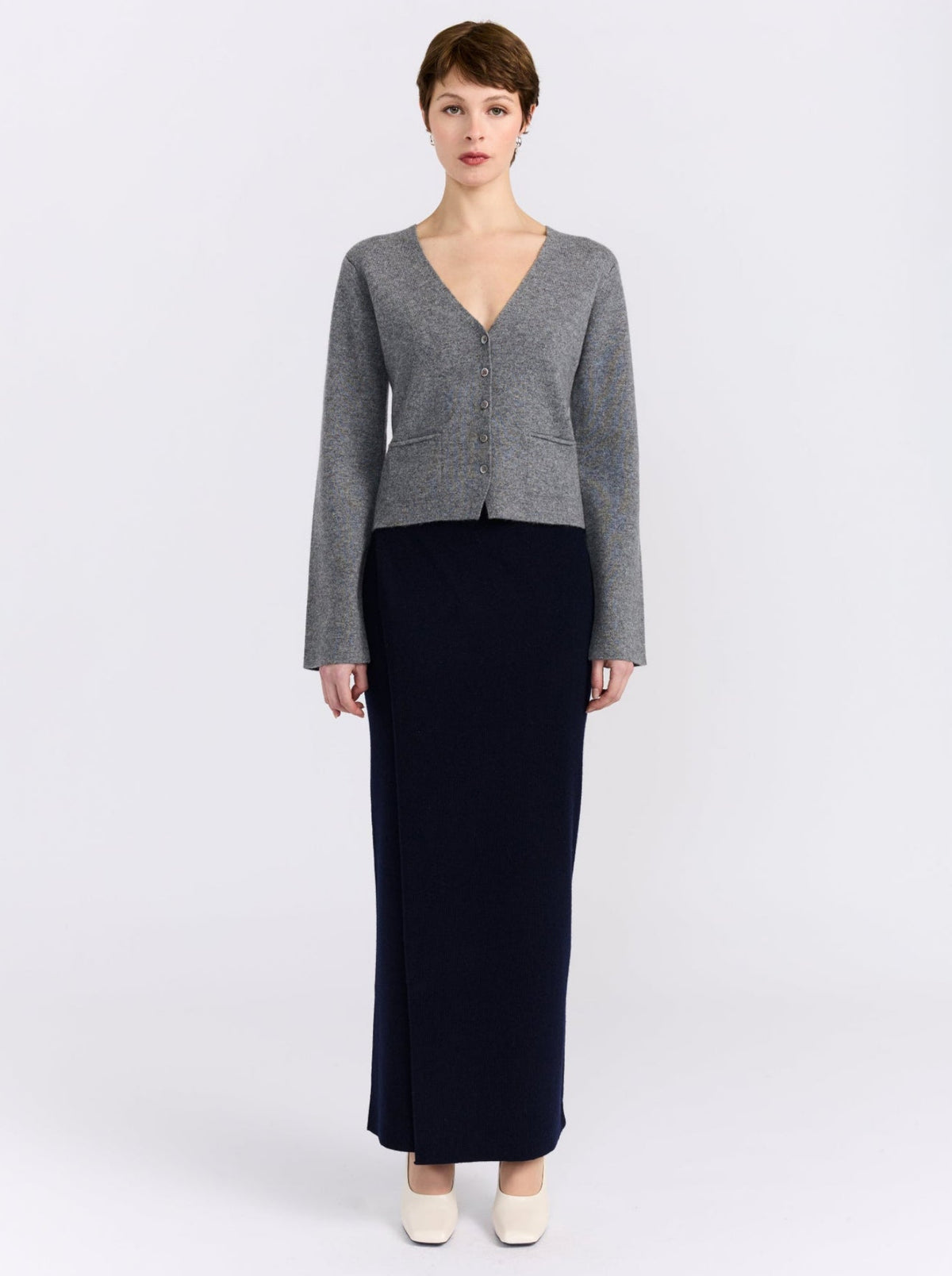 Front view model wears grey cashmere v neck button front cardigan with maxi length navy, straight skirt and white shoes.