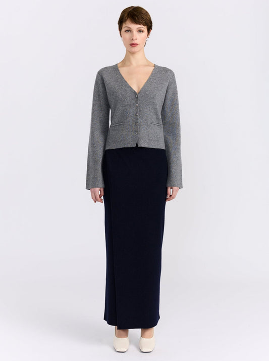 Front view model wears grey cashmere v neck button front cardigan with maxi length navy, straight skirt and white shoes.