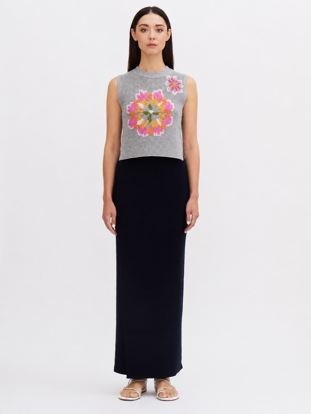 Woman wearing a sleeveless gray top with a colorful floral design and a long black skirt on a white background