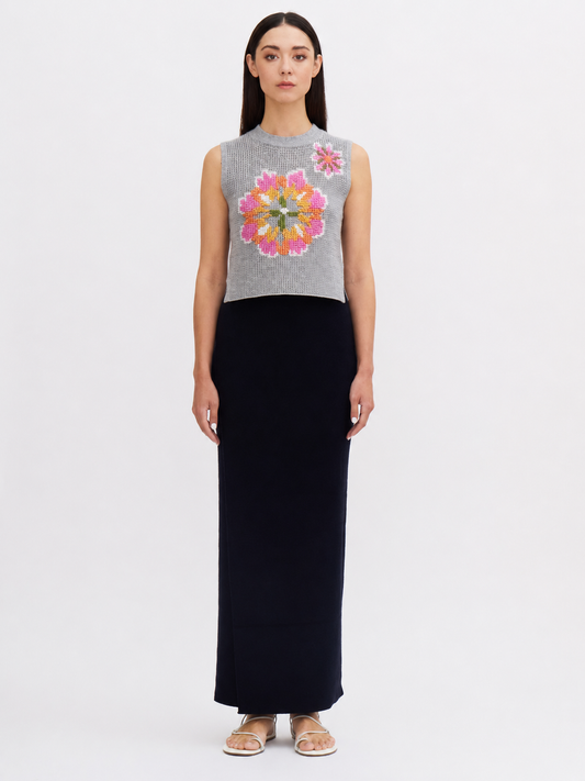 Woman wearing a sleeveless gray top with a colorful floral design and a long black skirt on a white background