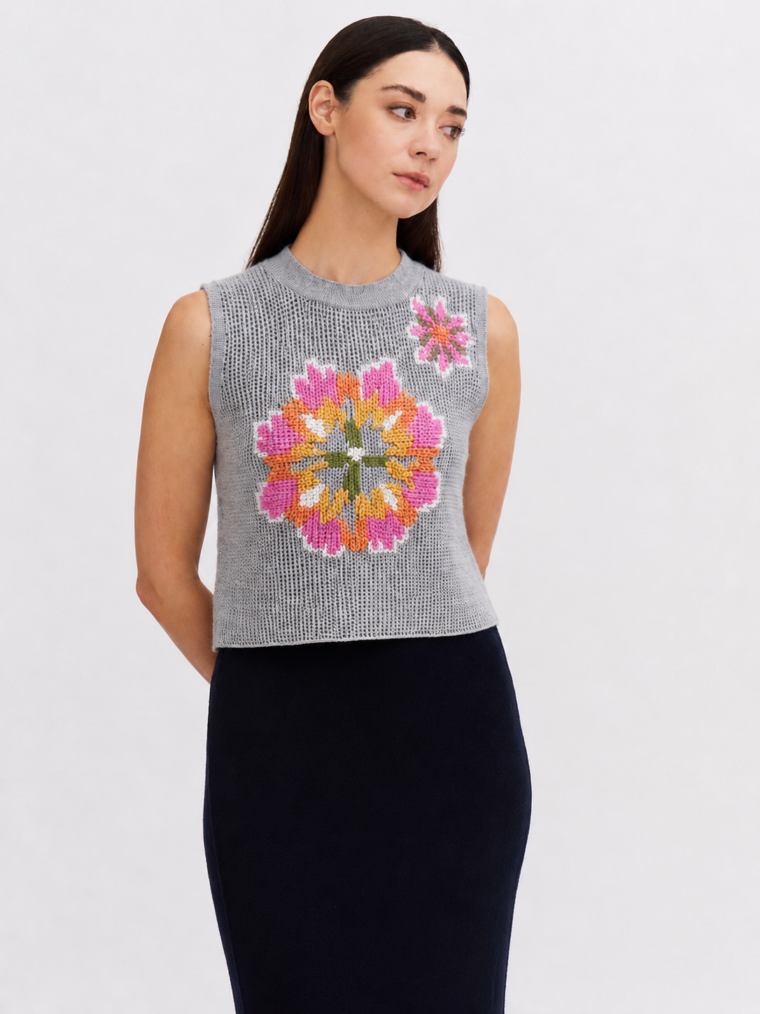Woman wearing a sleeveless gray knit top with colorful floral pattern on a white background