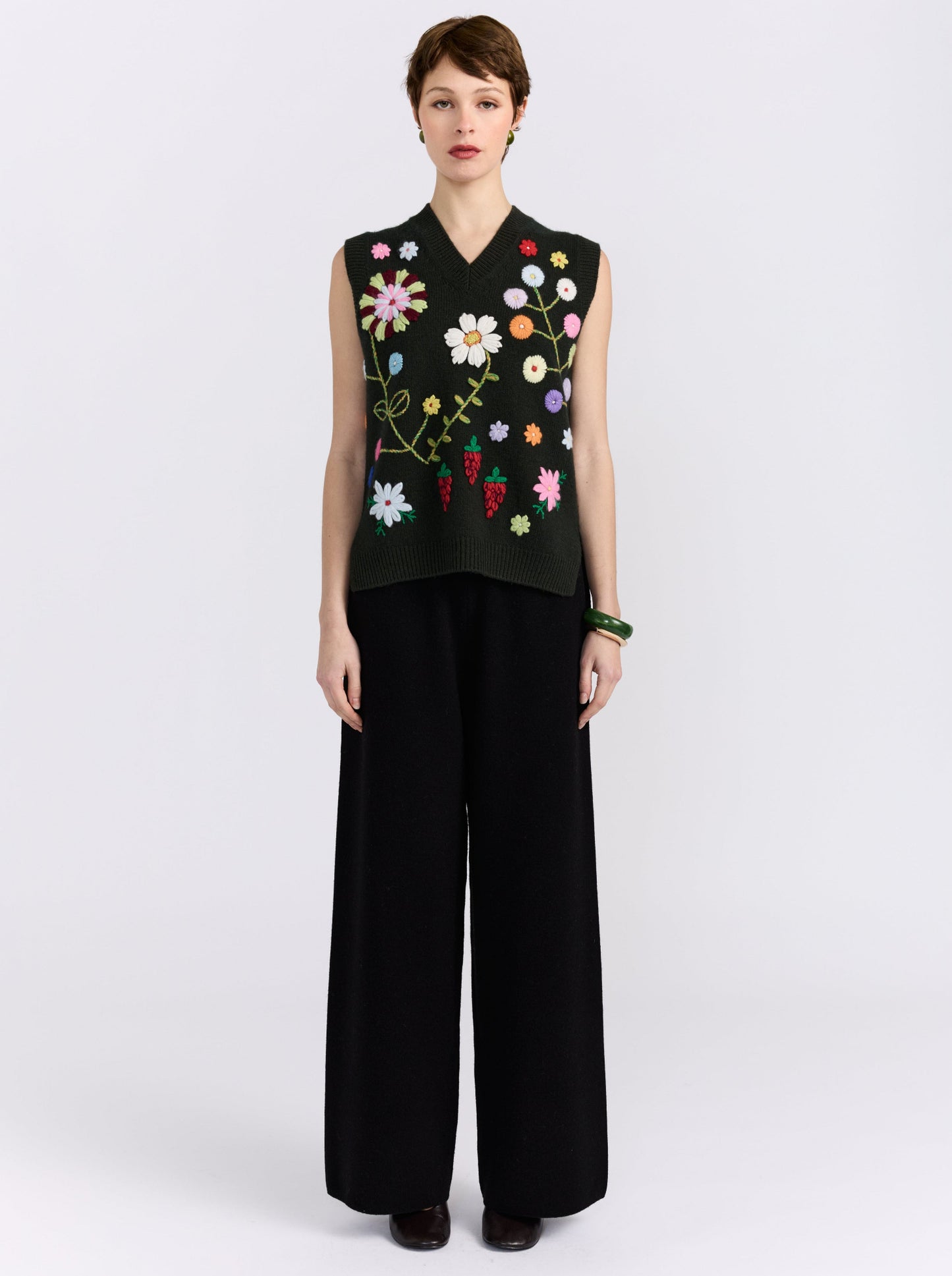 Khaki cashmere vest with hand-embroidered floral detailing, styled with black wide-leg trousers.