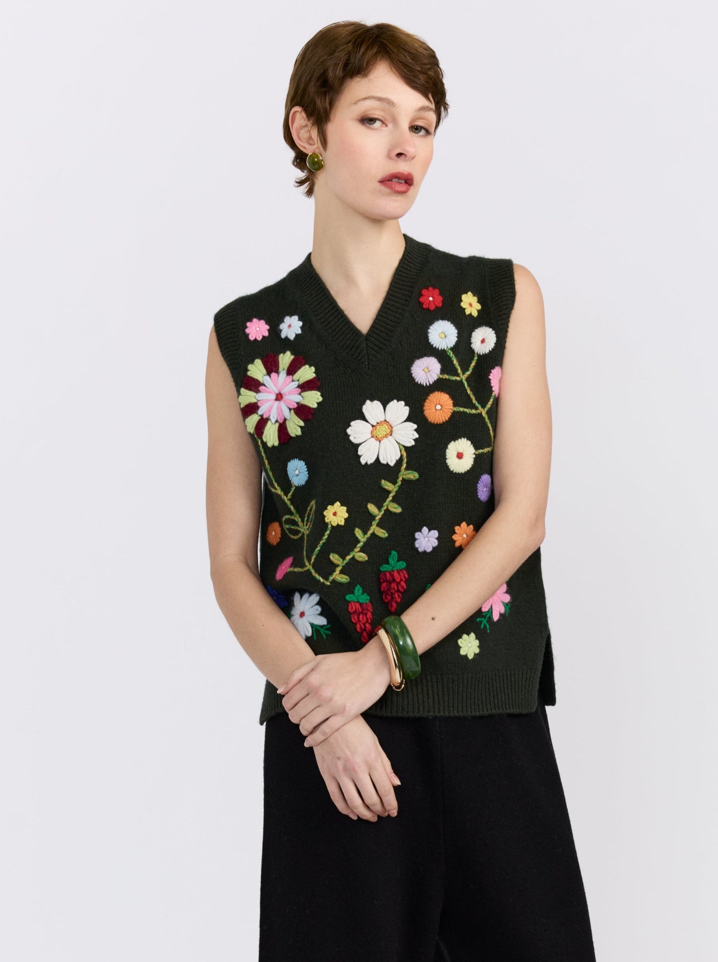 Khaki cashmere vest with hand-embroidered floral detailing, styled with black wide-leg trousers.