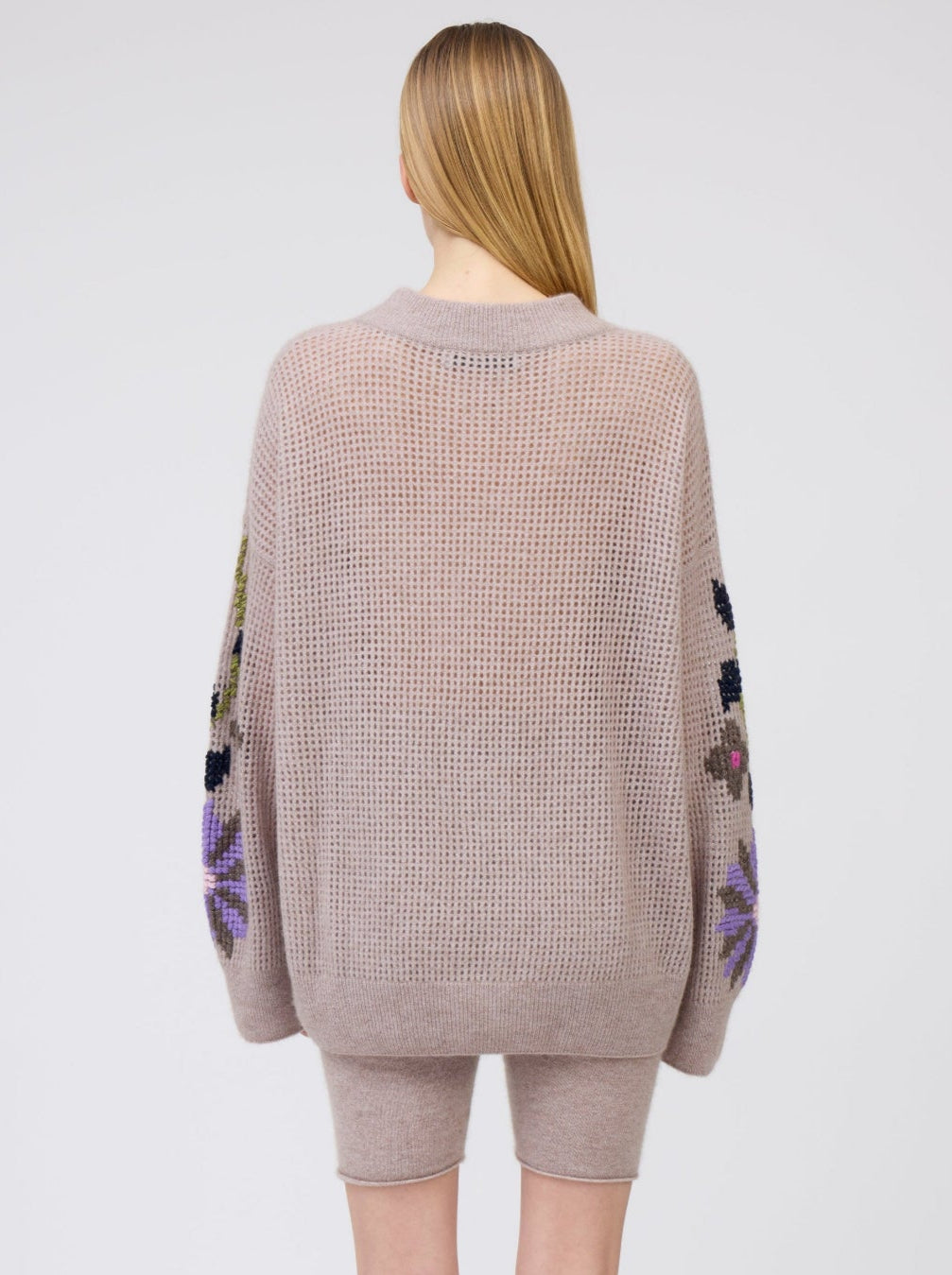 Back view of model wearing light weight beige cashmere net knit sweater, with round neck, long sleeves and worn with beige cashmere biker shorts.