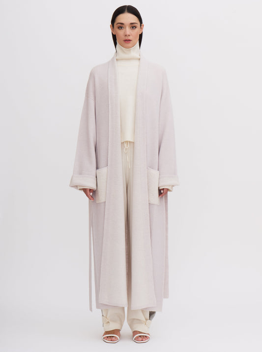 Front view of model wearing a pale lavender knitted cashmere long robe coat with contrast white lining and patch pockets.