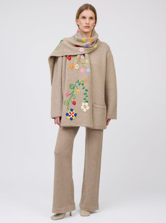 Front view model wearing light brown cashmere hip-length jacket with brightly coloured hand-embroidered scarf; worn with matching light brown knit pants.