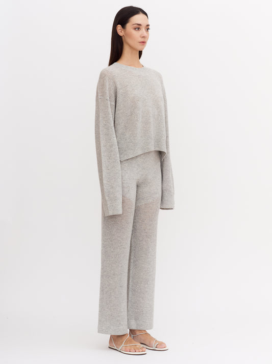 Model wearing light grey cashmere net knit wide leg pants with matching light grey, long sleeve net knit cashmere jumper.