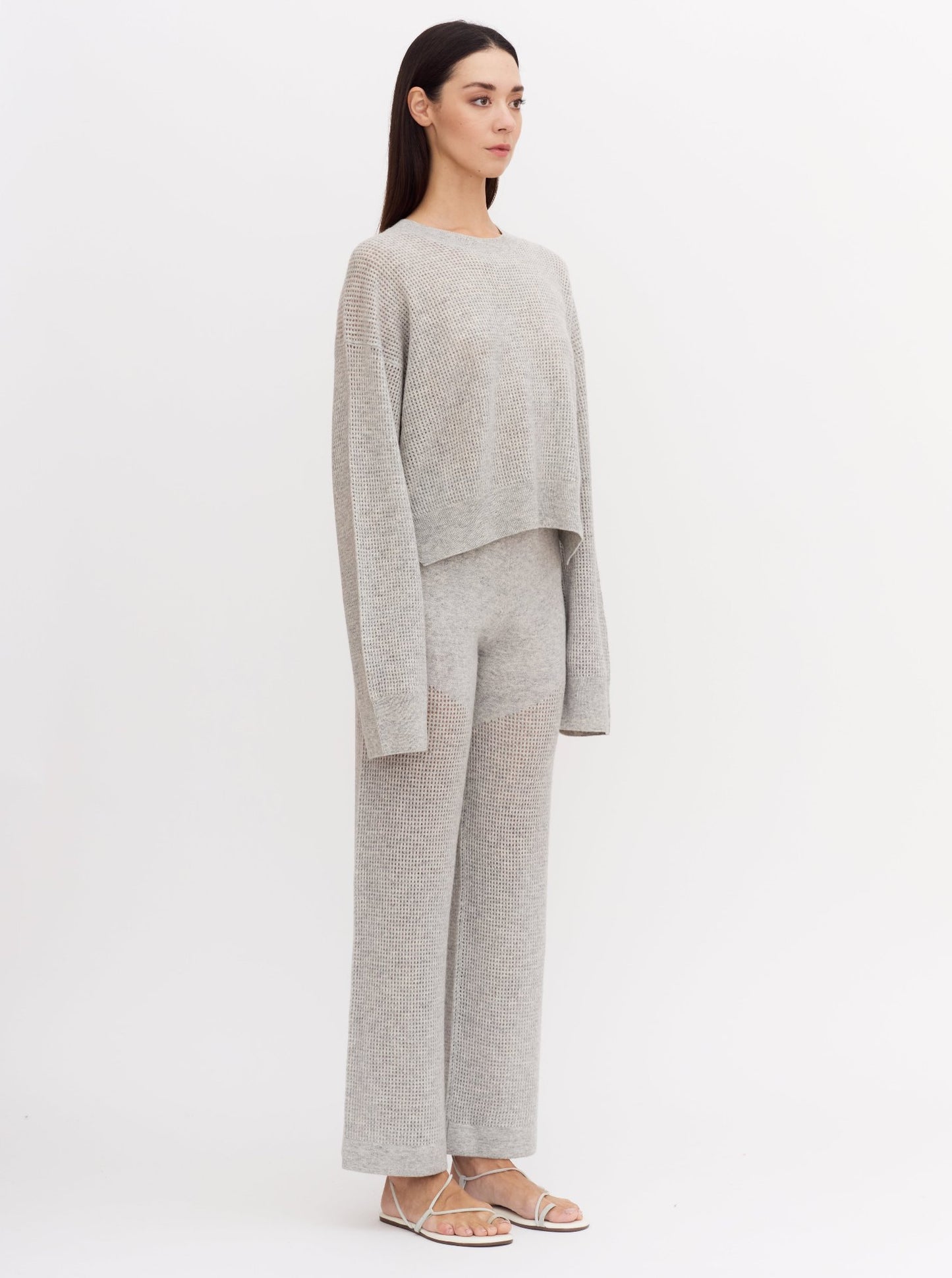 Model wearing light grey cashmere long sleeve net knit sweater with matching wide leg light grey pants.