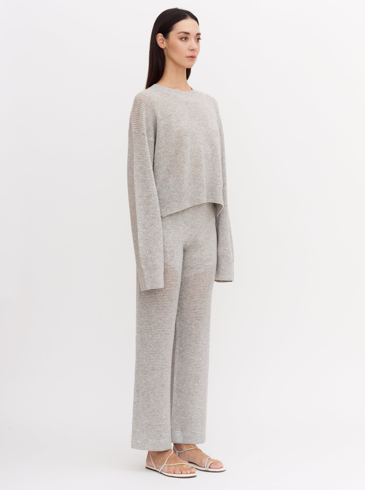 Model wearing light grey cashmere long sleeve net knit sweater with matching wide leg light grey pants.