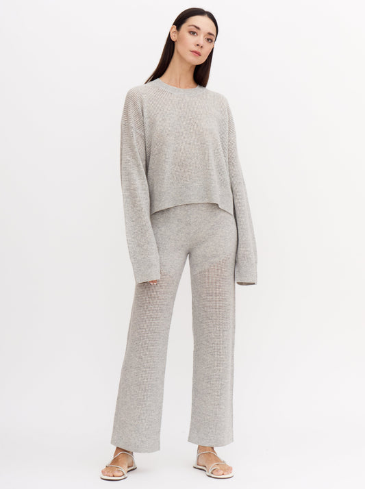 Relaxed front view of model wearing light grey, long sleeve, net knit cashmere sweater with matching cashmere net knit wide leg pants.