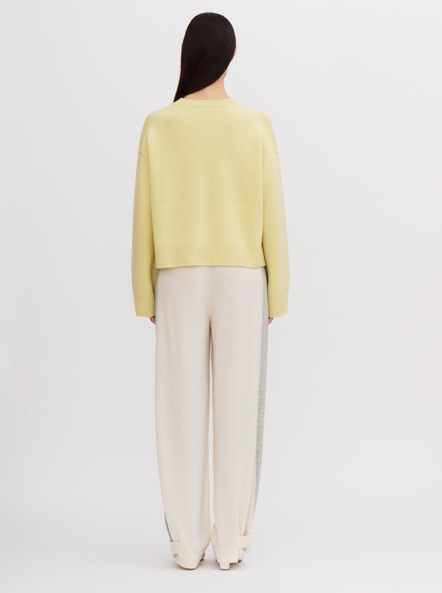 Light yellow cropped cashmere jumper with relaxed fit and wide sleeves, paired with cream trousers featuring grey side stripe.