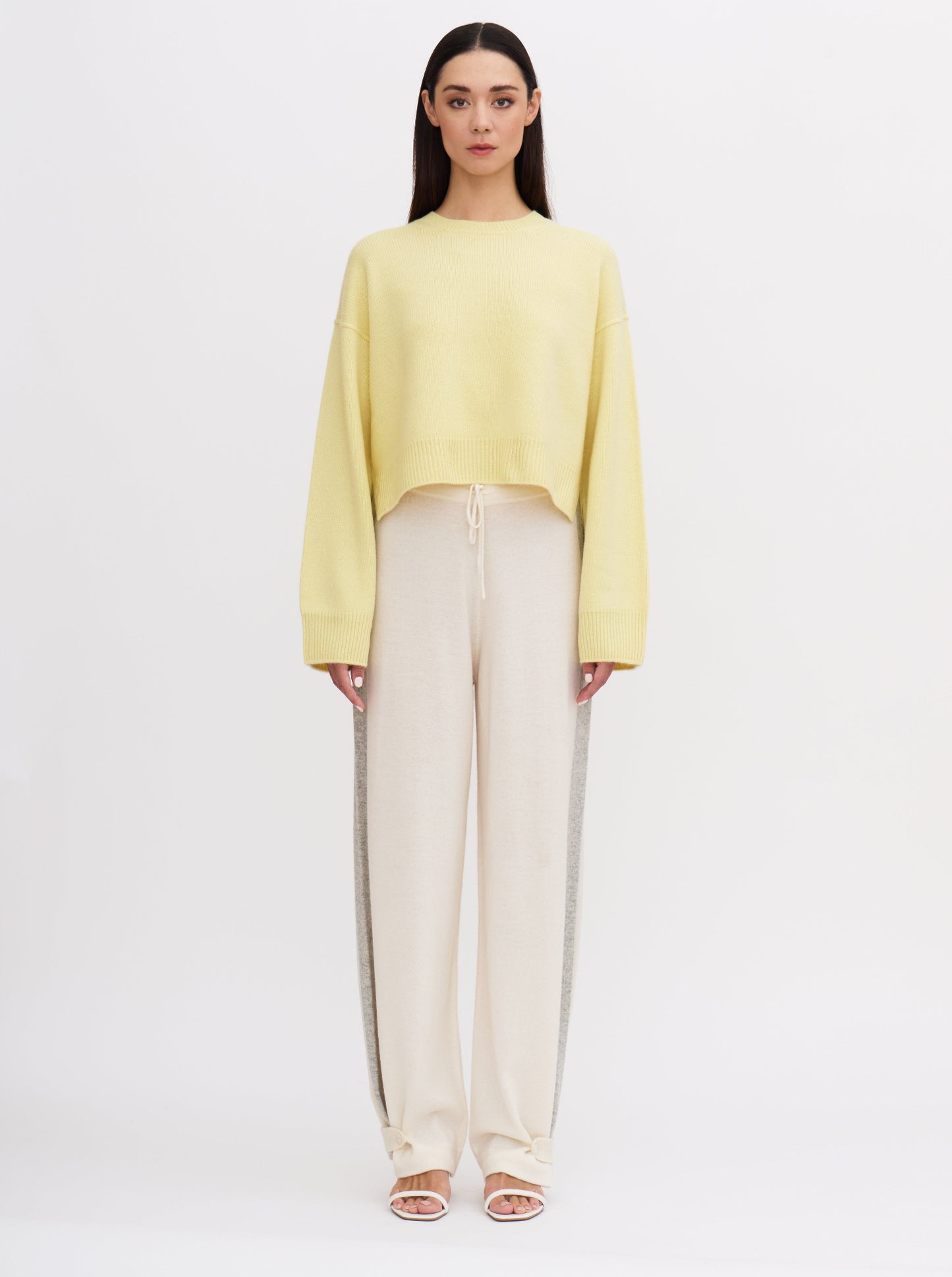 Light yellow cropped cashmere jumper with relaxed fit and wide sleeves, paired with cream trousers featuring grey side stripe.