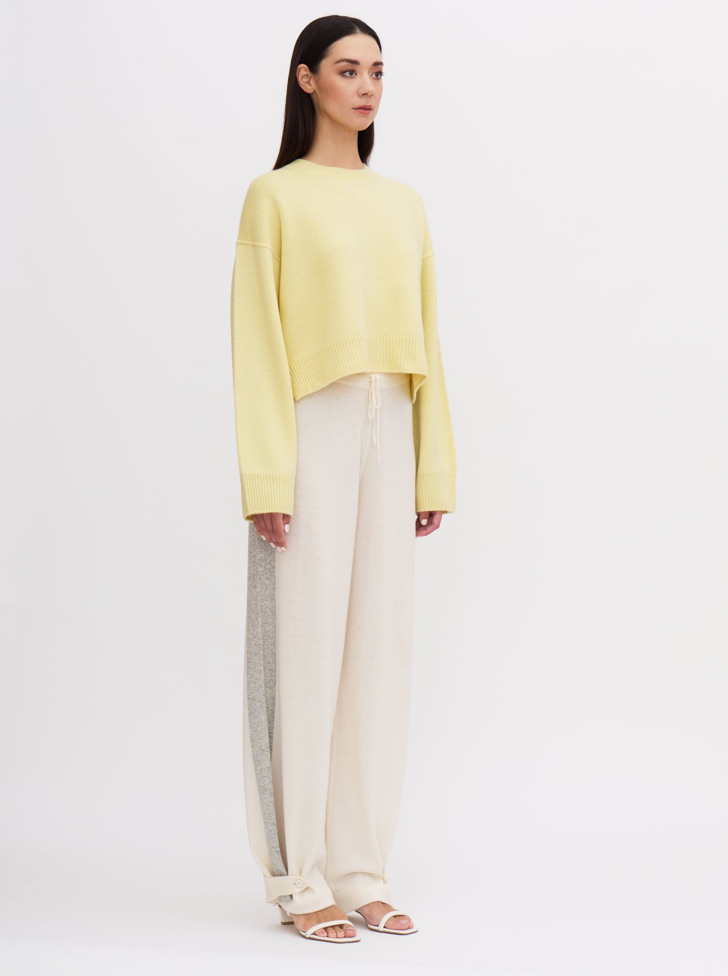 Light yellow cropped cashmere jumper with relaxed fit and wide sleeves, paired with cream trousers featuring grey side stripe.