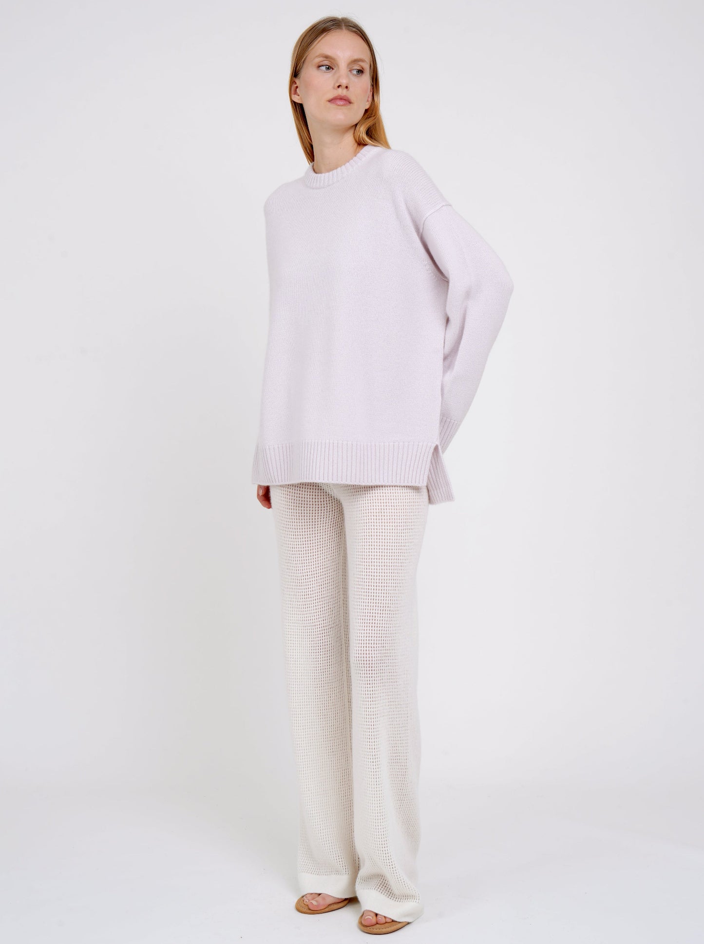 Standing model posing in pale purple long jumper with round neck, long sleeves and white cashmere knit pants.