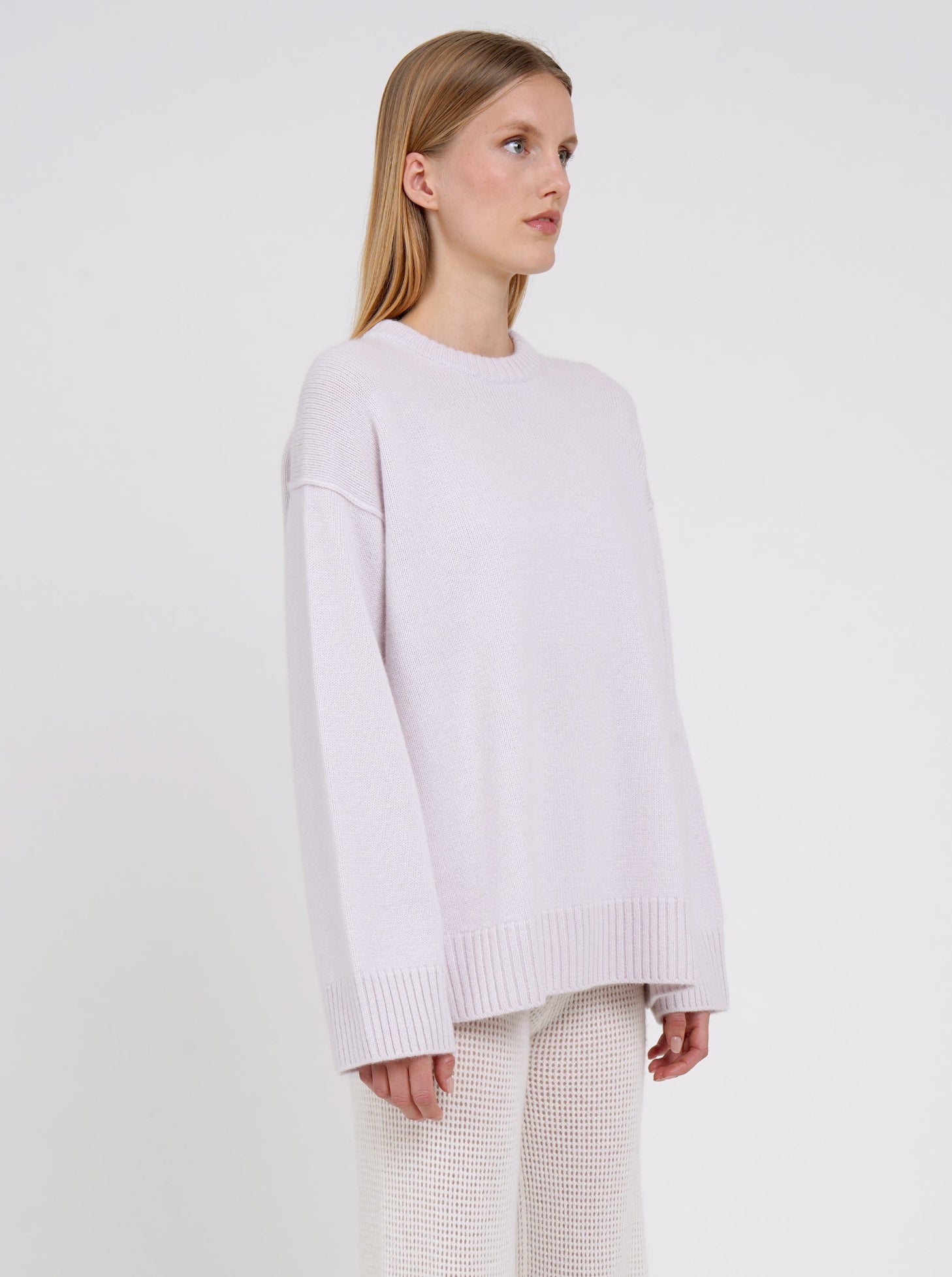 Close up side view model in pale purple long jumper with round neck, long sleeves and white cashmere knit pants.