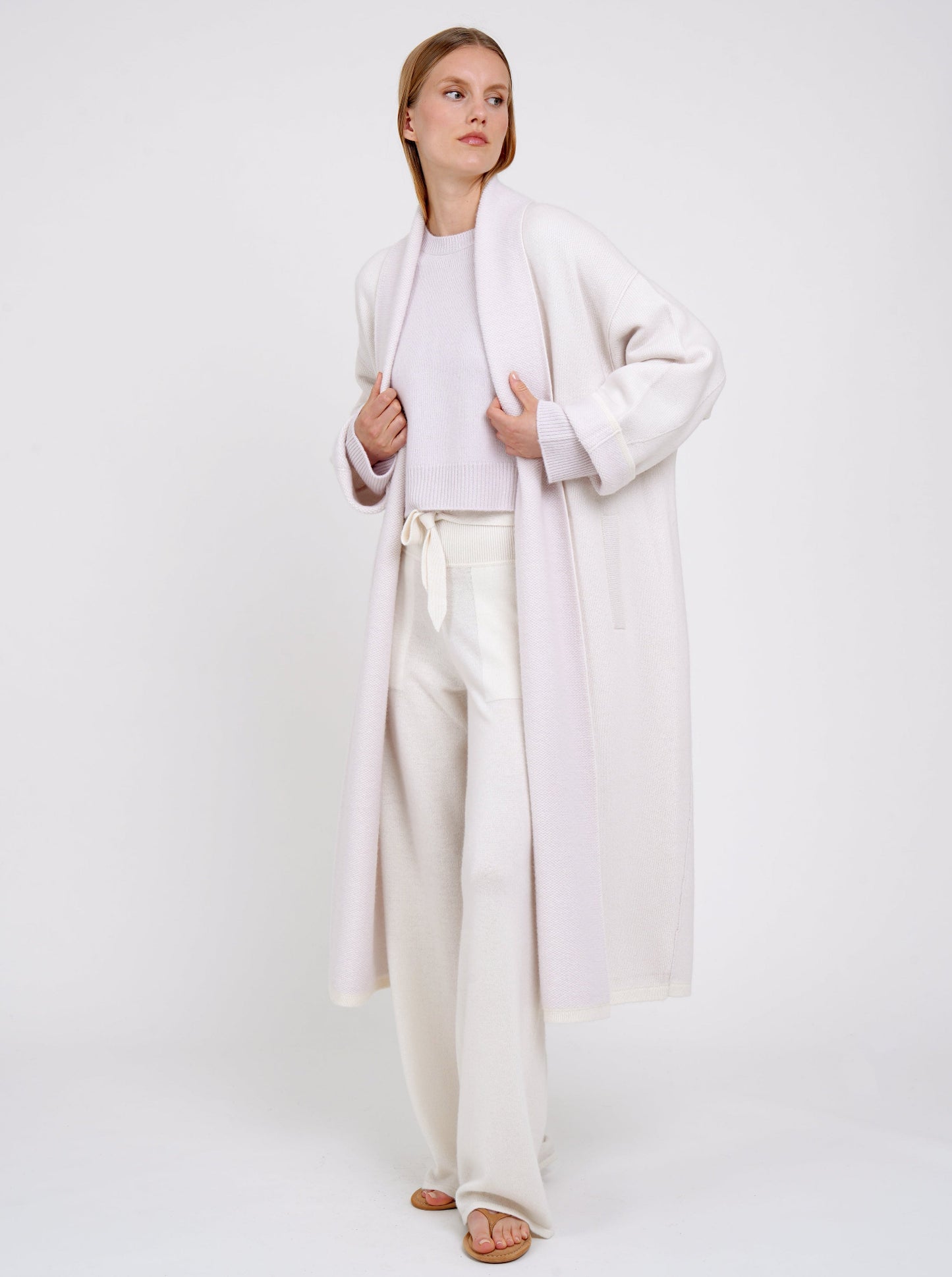 Model wears lilac and white mix cashmere knit coat with lilac collar revere and turn back cuffs; wearing with lilac cropped jumper and wide leg white cashmere pants.